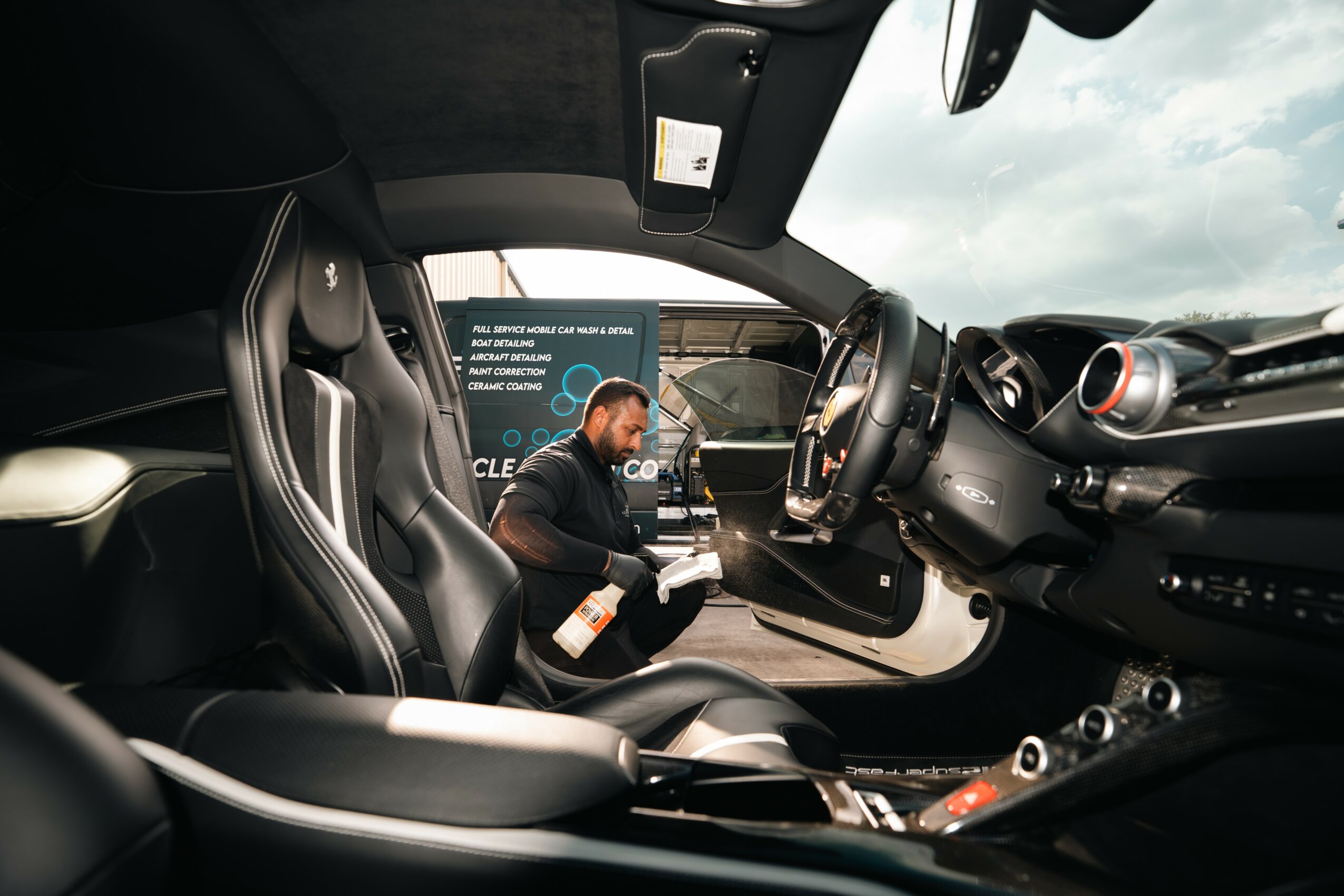 Interior of a car with a person sitting in the driver's seat, holding a drink, and looking at a screen outside the window.
