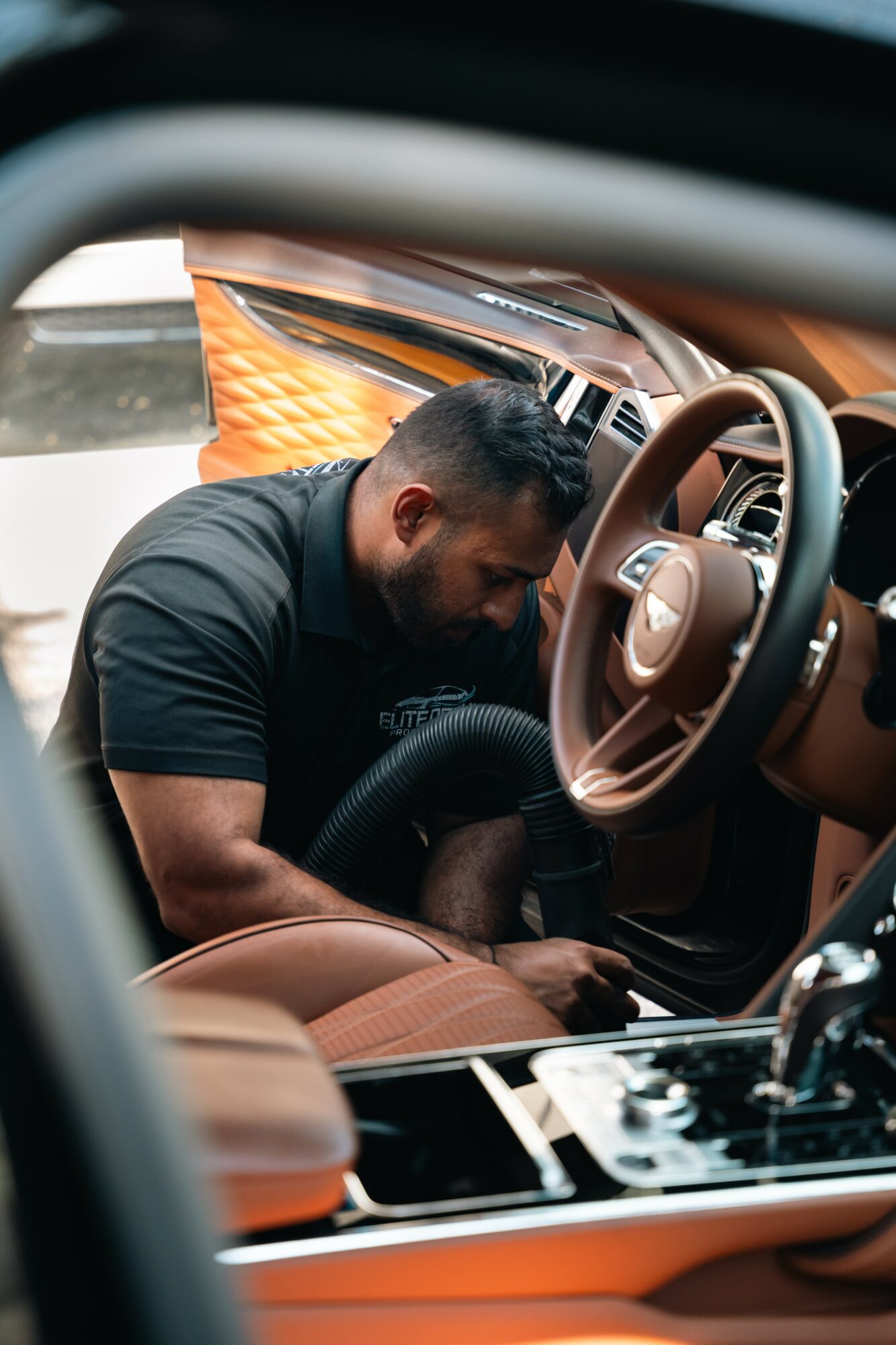 Man sitting inside a car, leaning forward, with the steering wheel and dashboard visible.