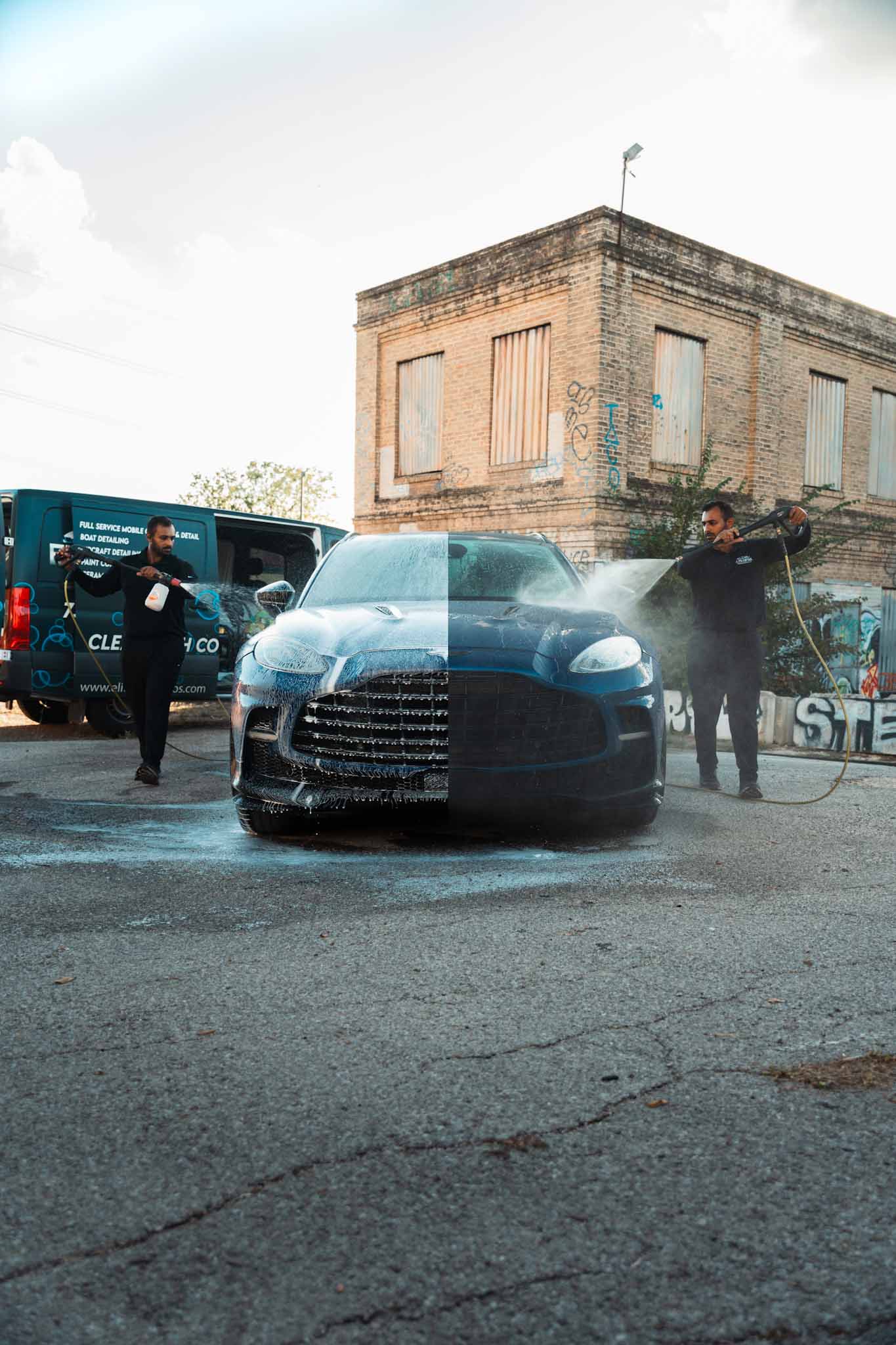 Black sports car with people standing nearby, one person pointing, in front of a building and a van, daytime.
