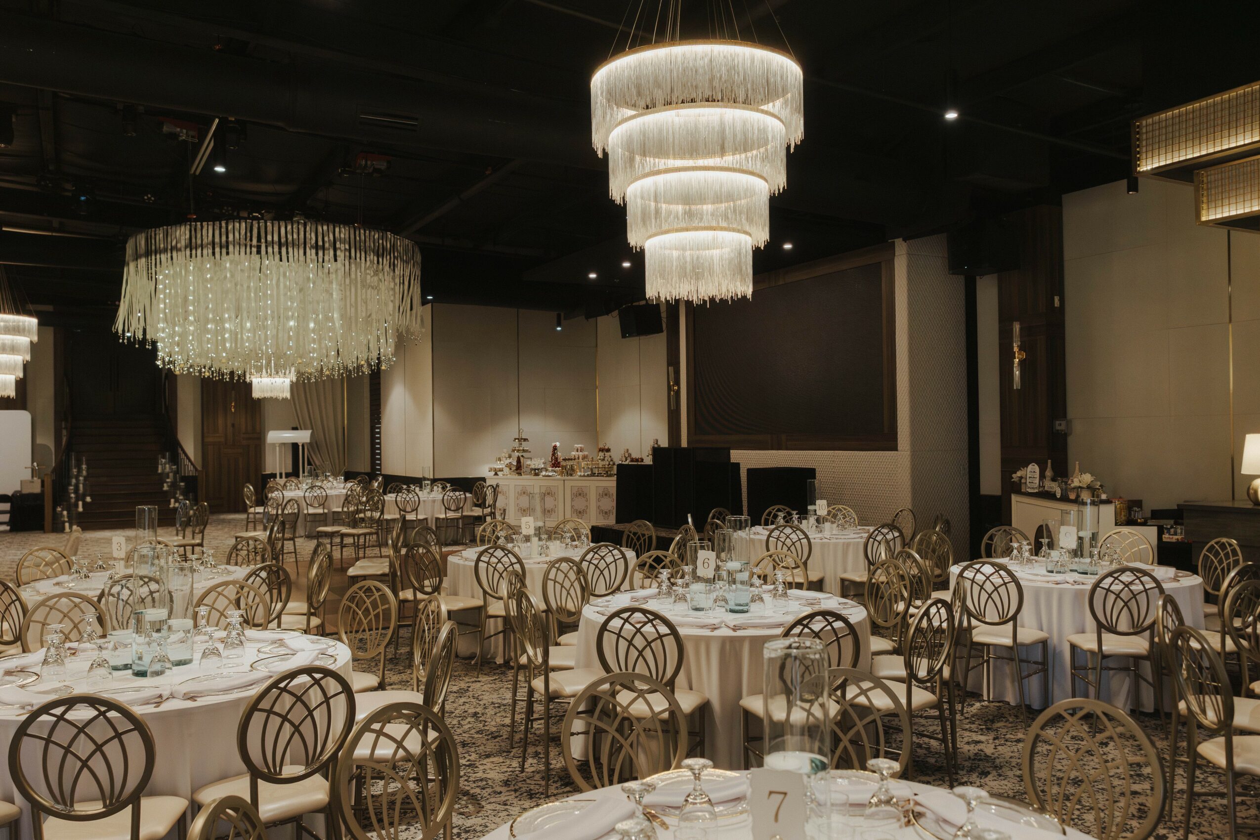 Elegant banquet hall with chandeliers, round tables, and chairs, set for an event with tableware and decorations.