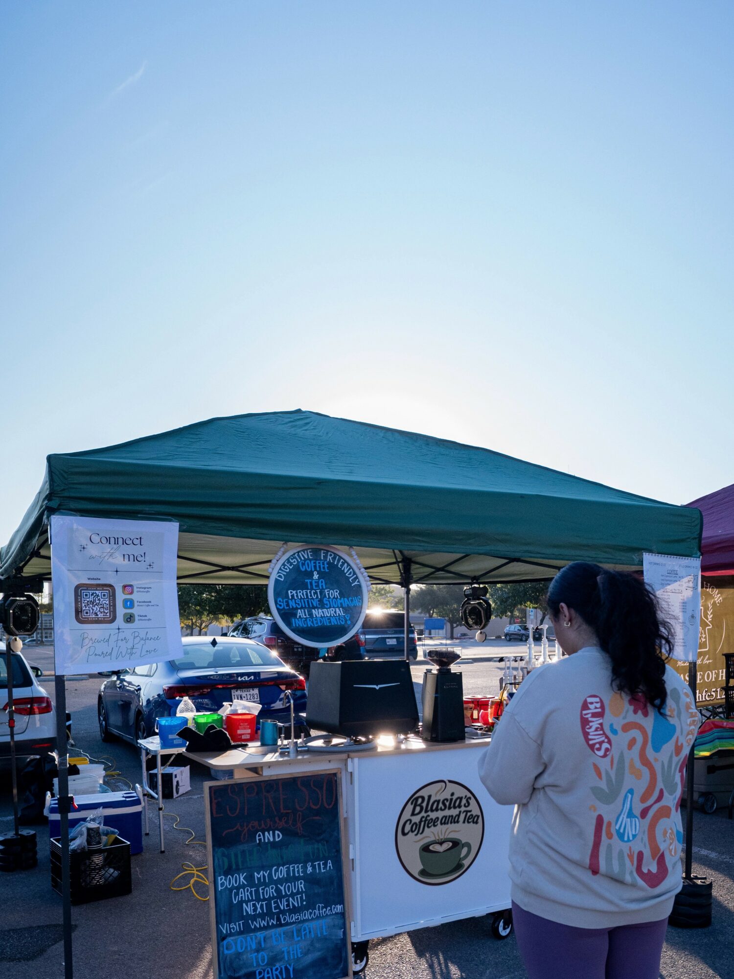 Person standing near a market stall with a green canopy, various items, and a sign for Blasman's Coffee.