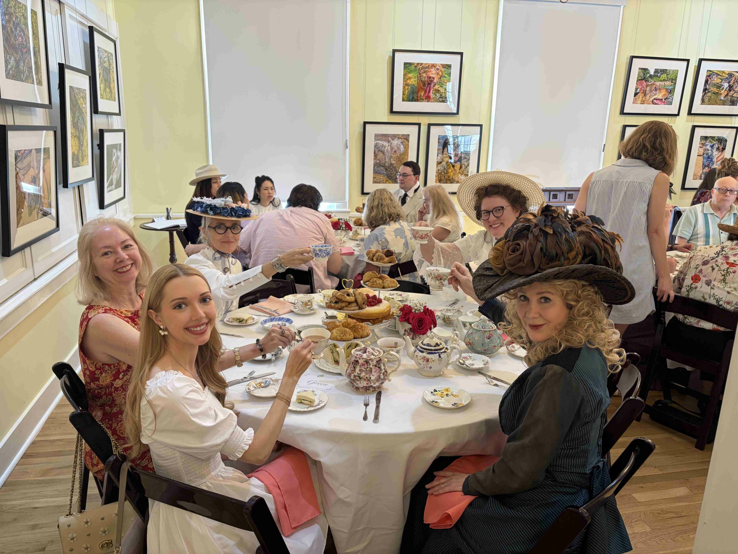 People gathered around a table at an art gallery, enjoying food and drinks, with framed artwork on the walls.