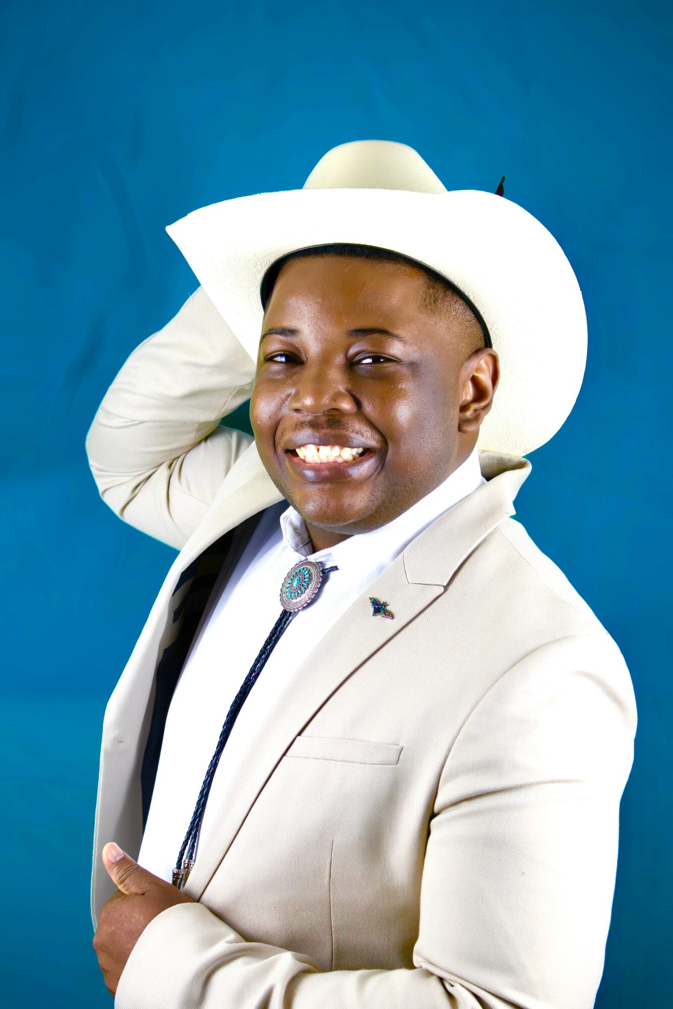 Person wearing a white hat and suit, smiling, against a blue background.