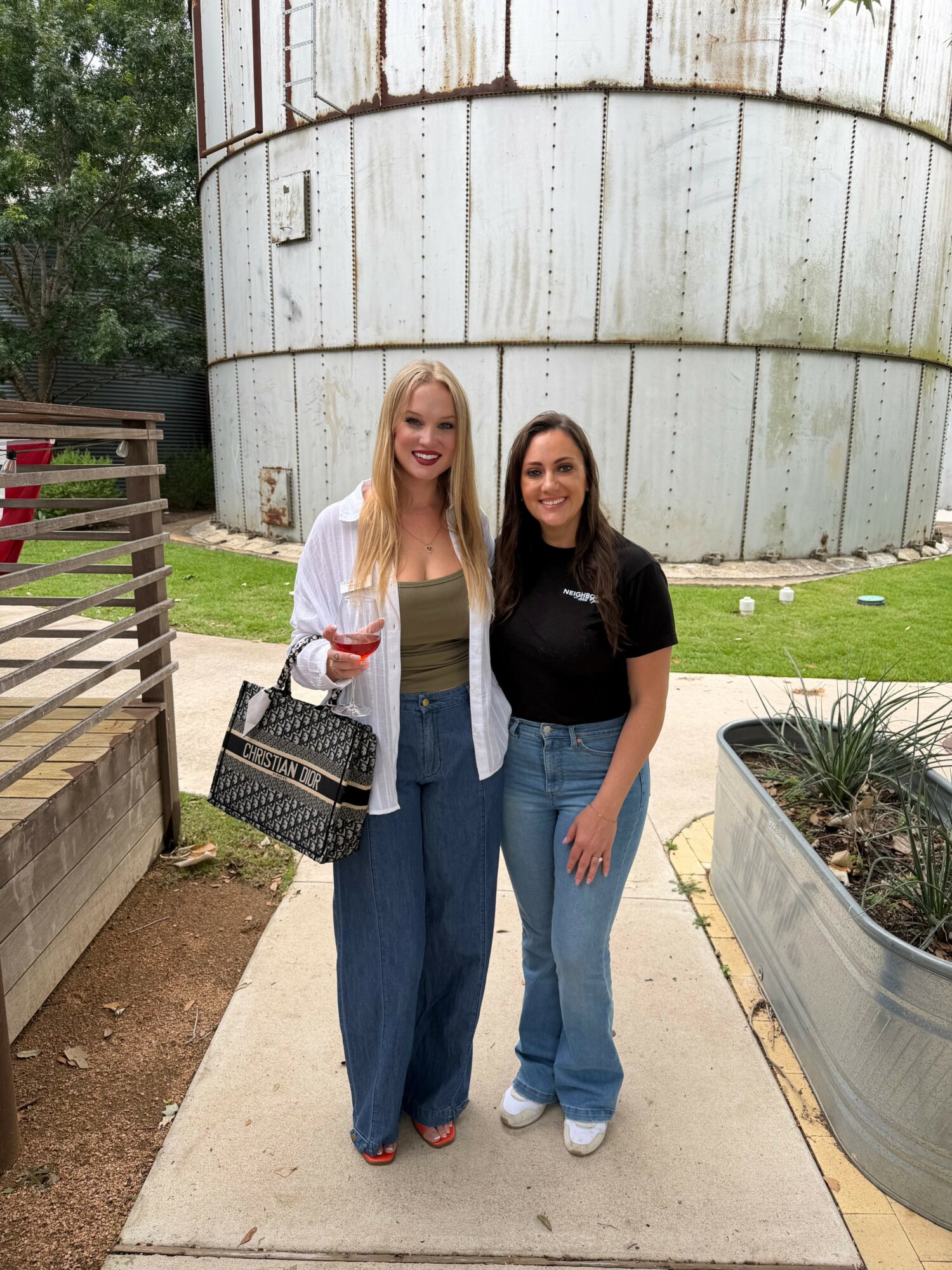 Two women stand outdoors in front of a large, curved metal structure, smiling and posing for the photo.