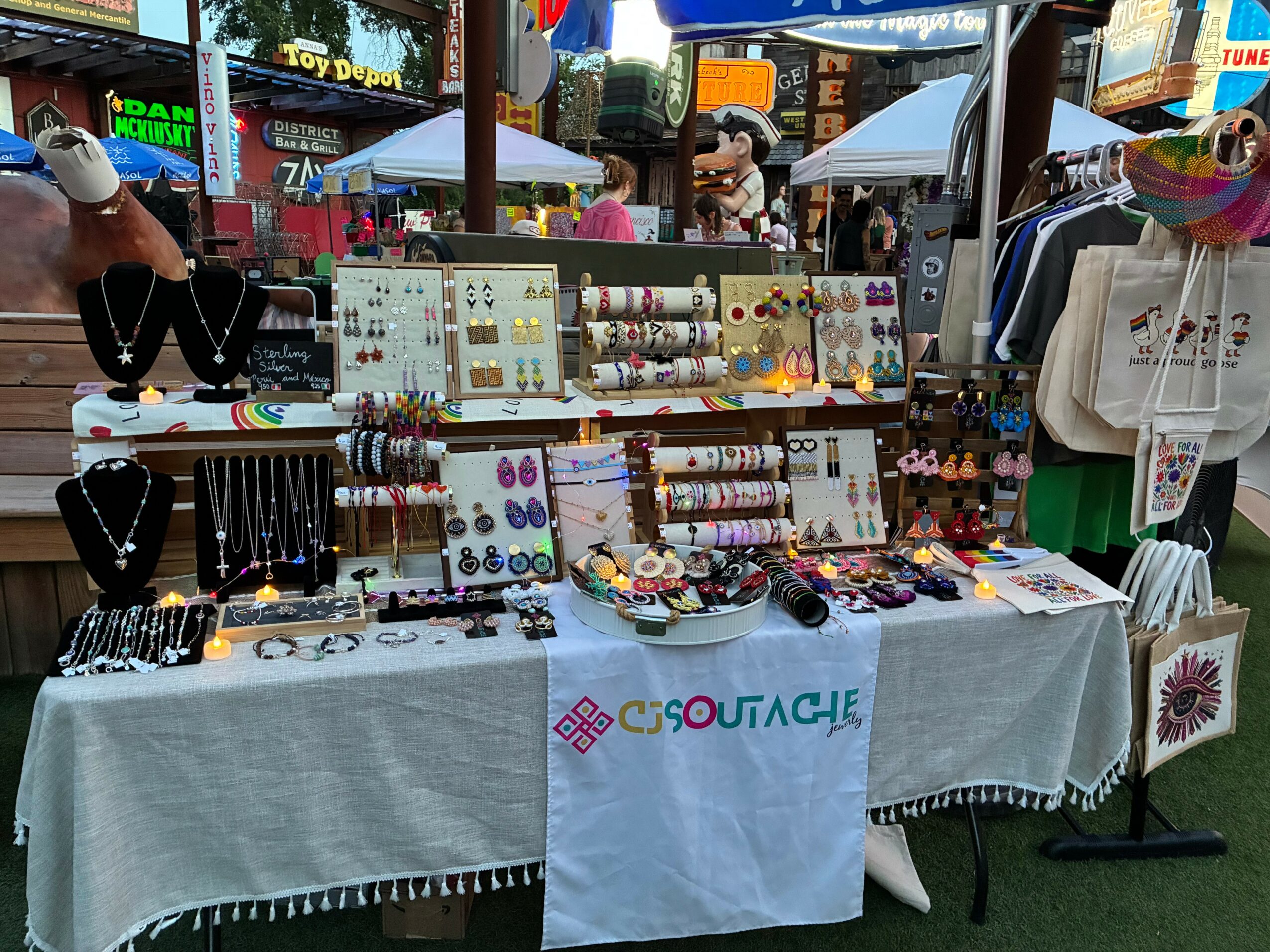 Jewelry and accessories display at an outdoor market stall with colorful items and signs in the background.