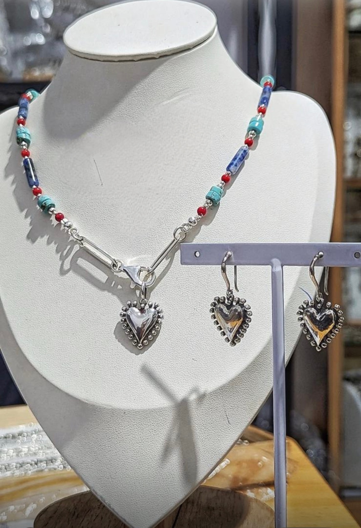 Beaded necklace with heart-shaped pendant and matching earrings displayed on a white jewelry bust.
