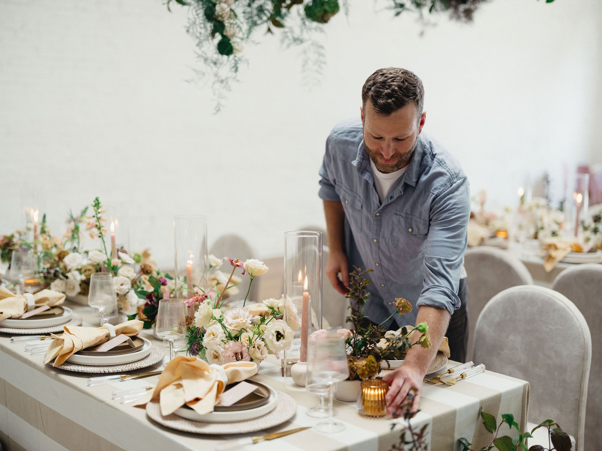 Man arranging a decorated table with flowers and tableware at an event, smiling and leaning forward.
