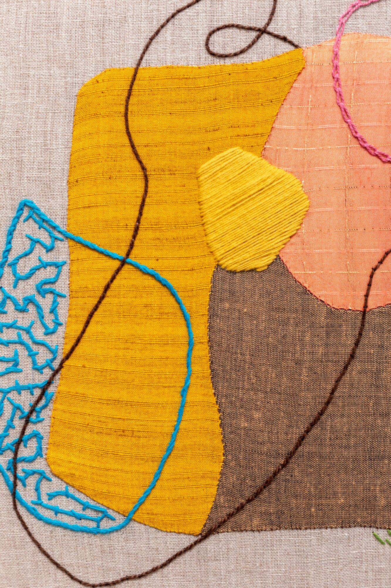 Close-up of colorful embroidered fabric with yellow, pink, brown, and blue threads, and visible stitching details.