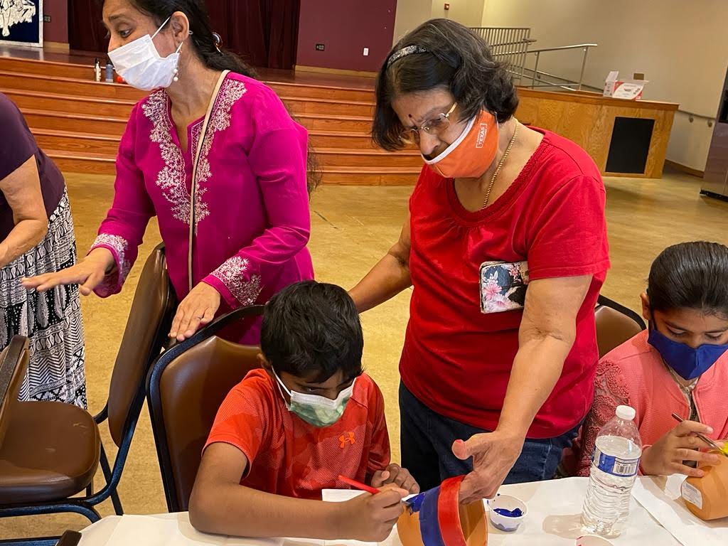 Two women and two children wearing masks in a classroom, engaging in an activity at a table with water bottles.