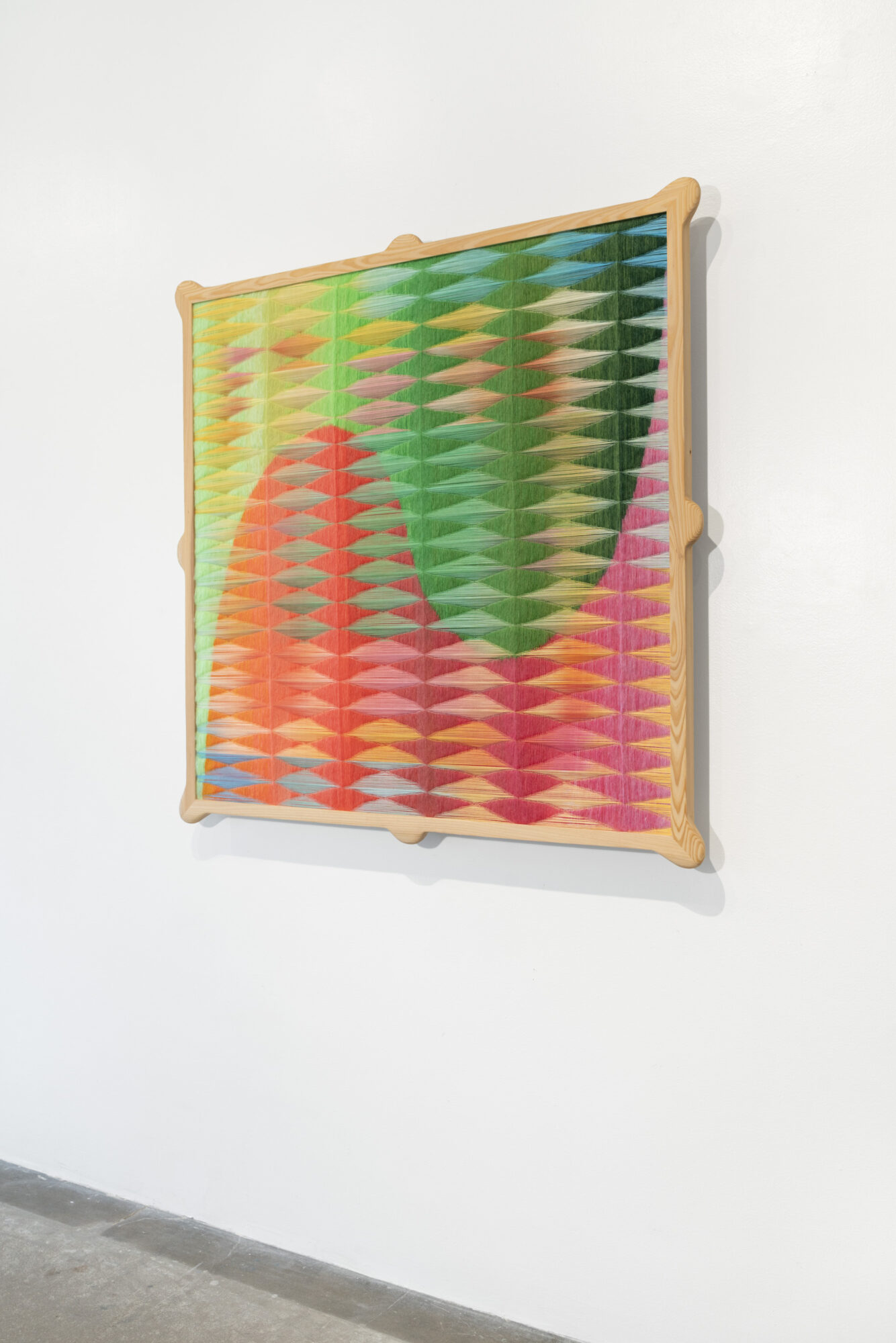 Colorful geometric wall art with a pattern of overlapping ovals in various colors, mounted on a white wall.