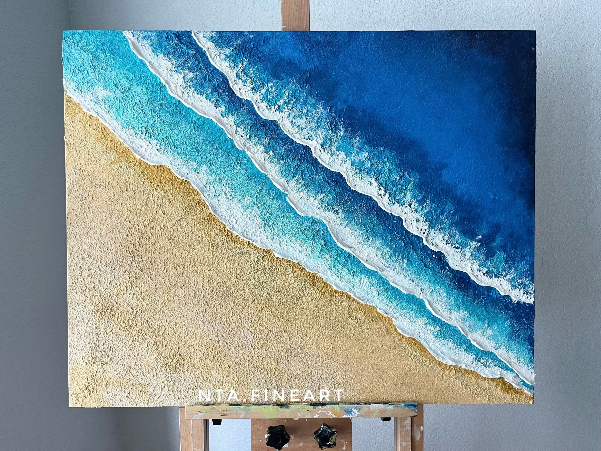 Painting of a beach with waves crashing onto the sandy shore, blue sky in the background.