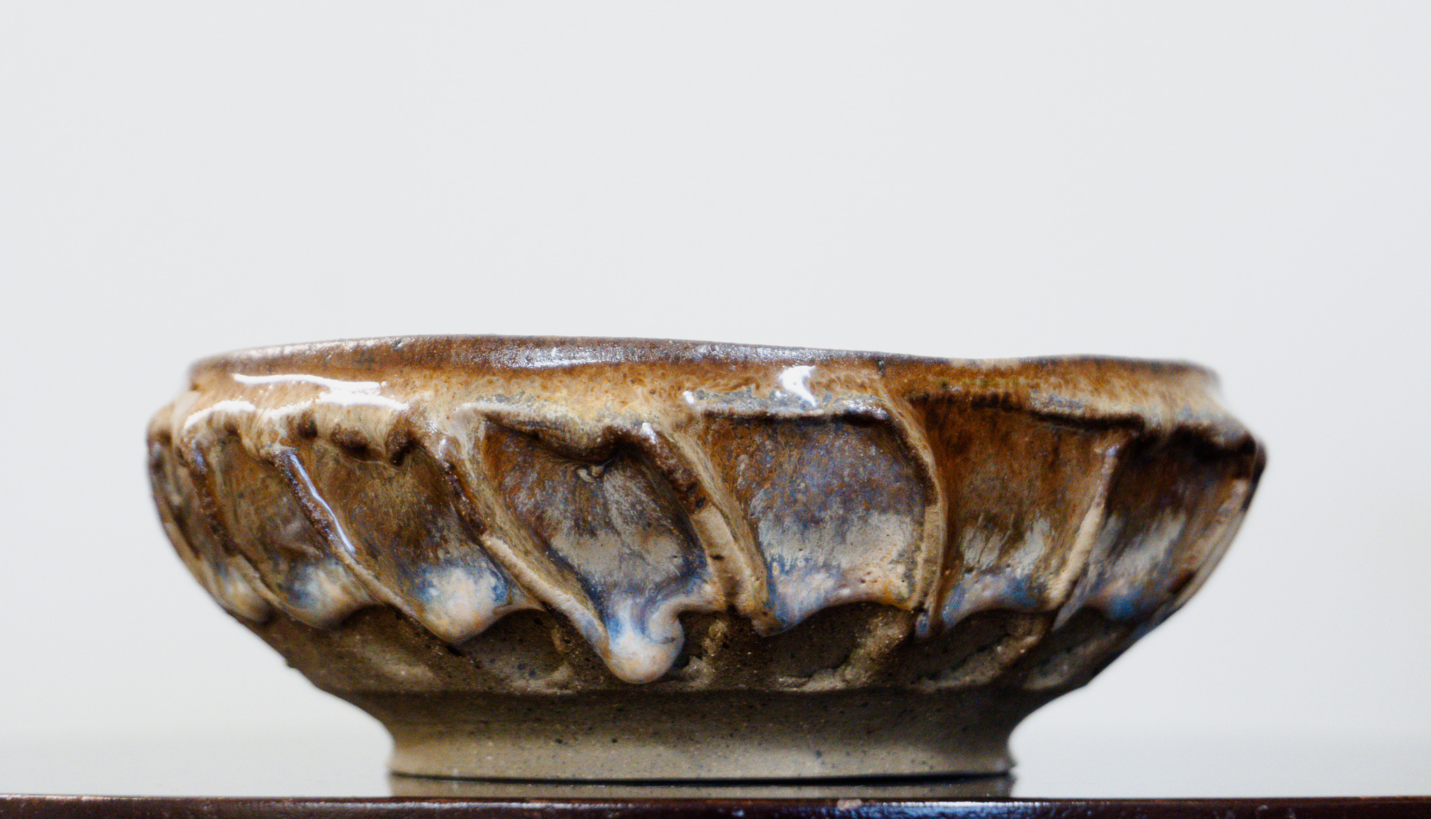 Close-up of a ceramic bowl with a textured, glazed surface, placed on a dark stand against a plain background.