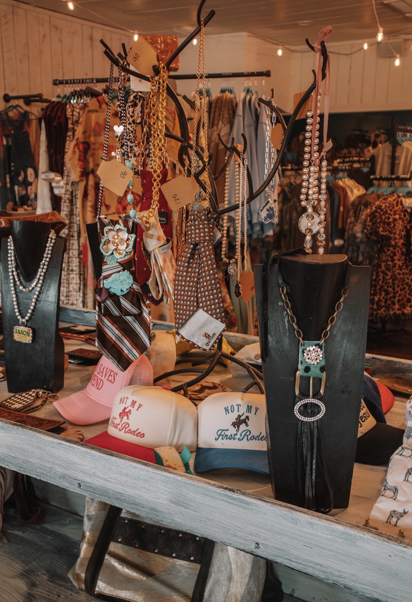 Display of jewelry and accessories on black busts and tables at a market stall, with clothing in the background.