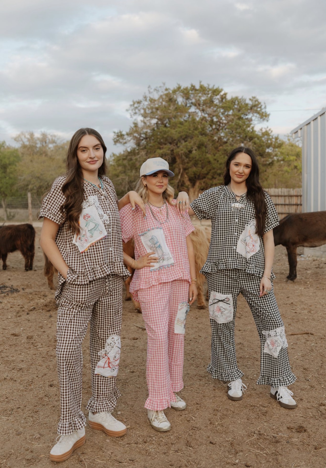 Three women in pajamas standing outdoors with animals and trees in background.