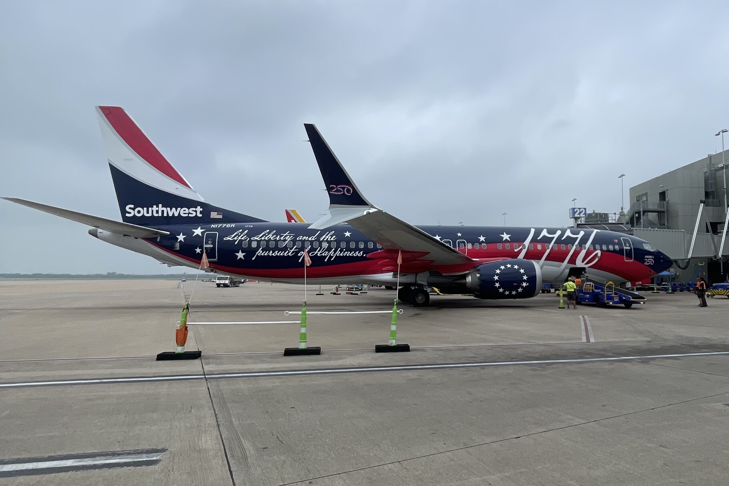 Airplane parked on tarmac with patriotic red, white, and blue design, surrounded by cones and airport buildings.