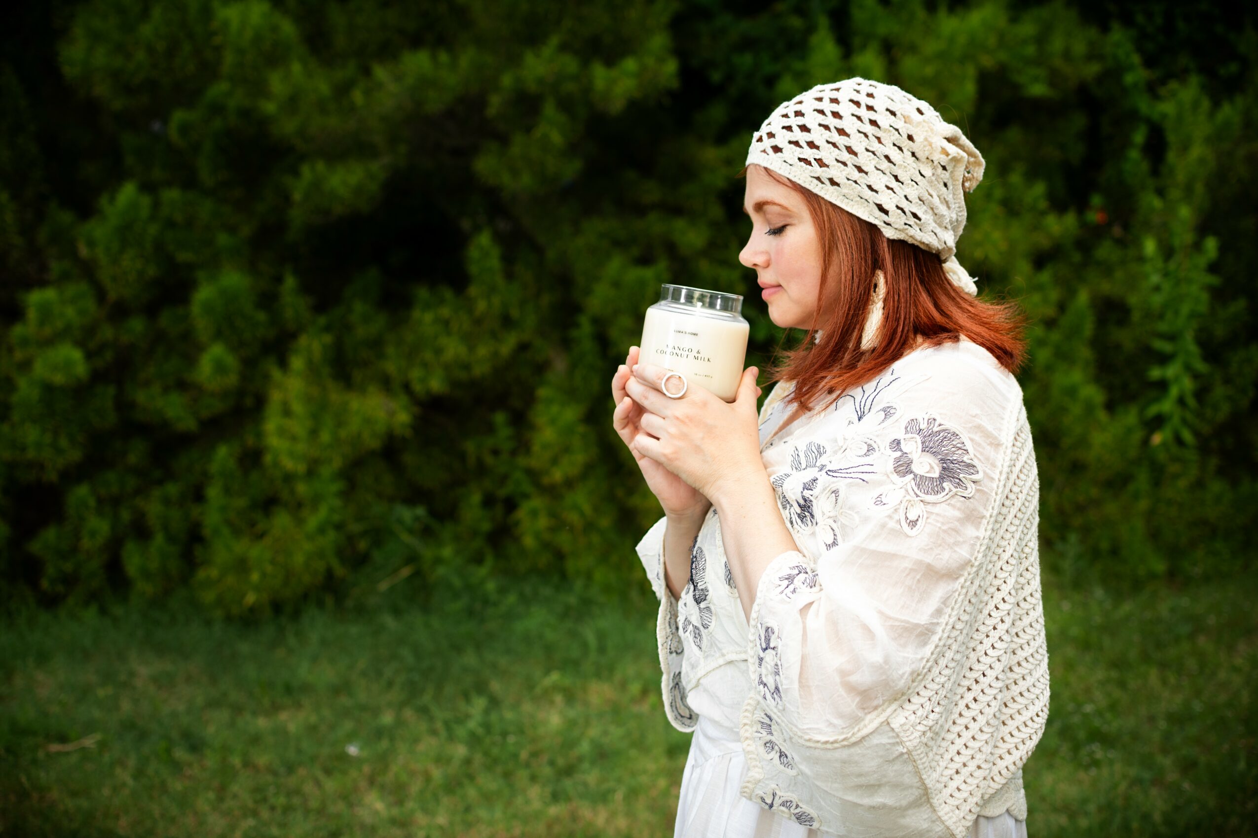 Woman with a patterned headscarf holding a glass of milk outdoors, green trees in background.
