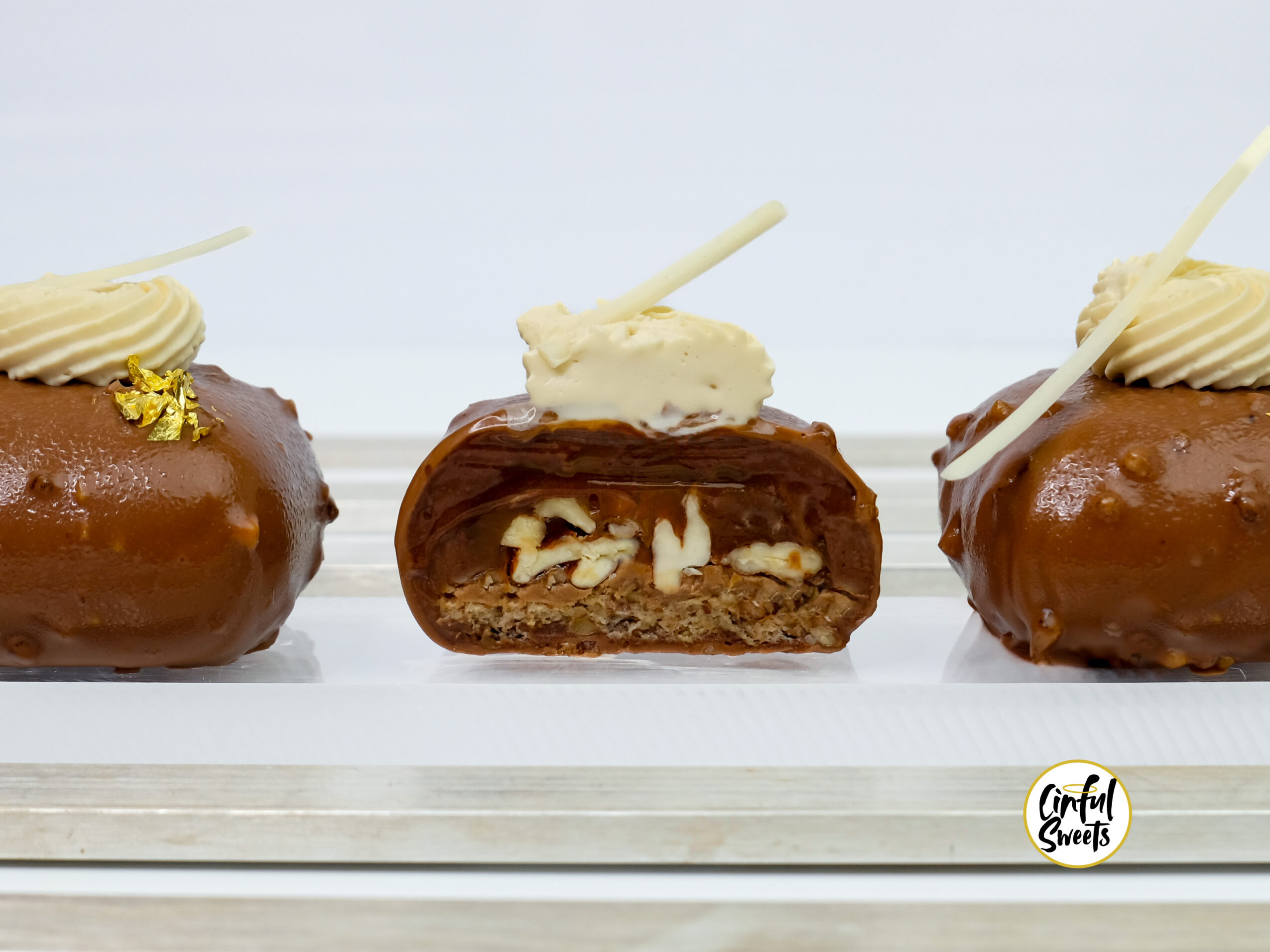 Three éclairs with cream toppings on a white surface, one cut in half showing filling, with a logo in the bottom right corner.