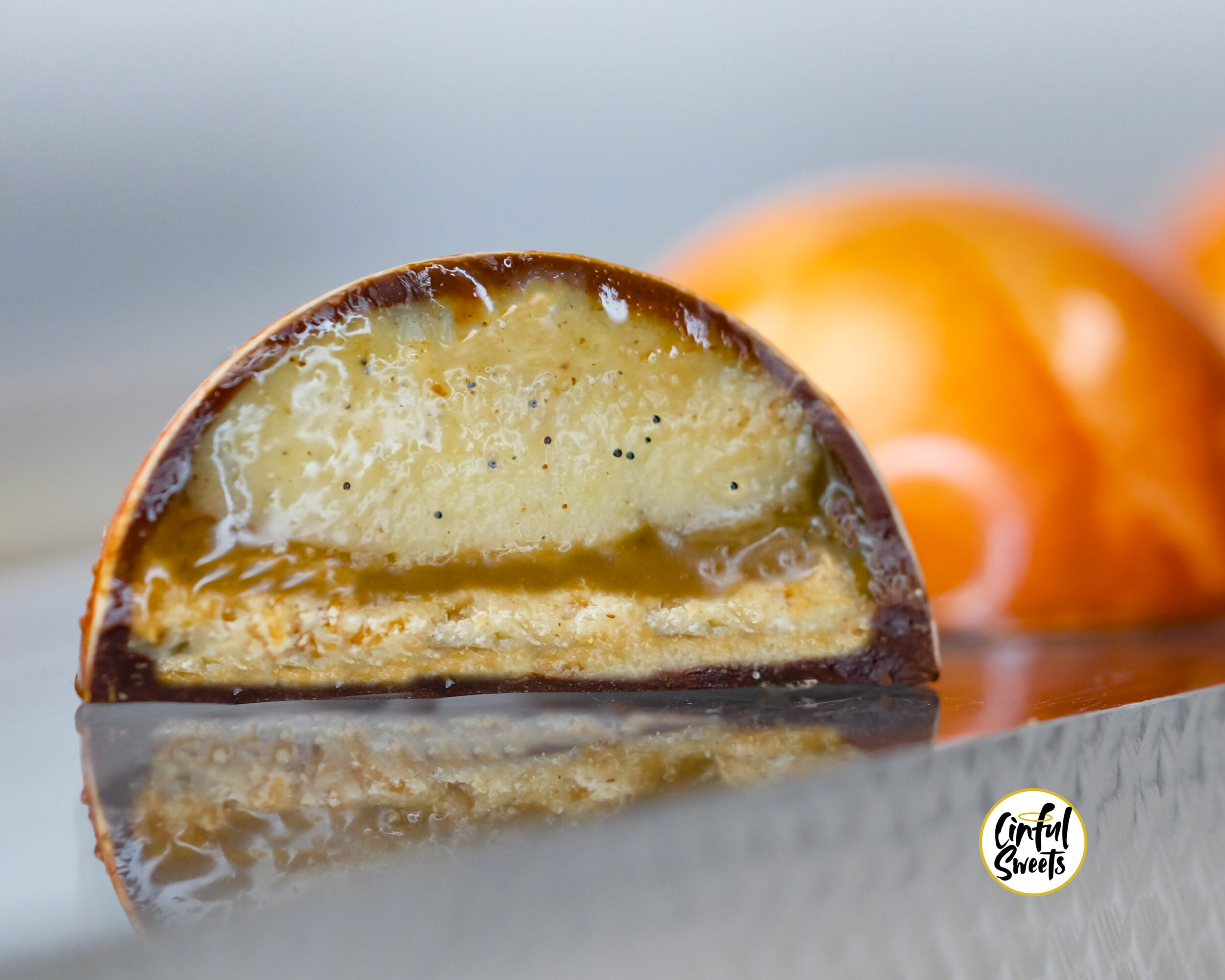 Close-up of a halved dessert with creamy filling and a shiny chocolate coating, with blurred pastries in background.