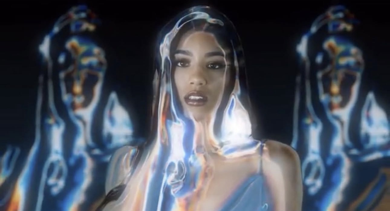 A woman with long dark hair and makeup touches her face, surrounded by abstract blue and white light patterns.
