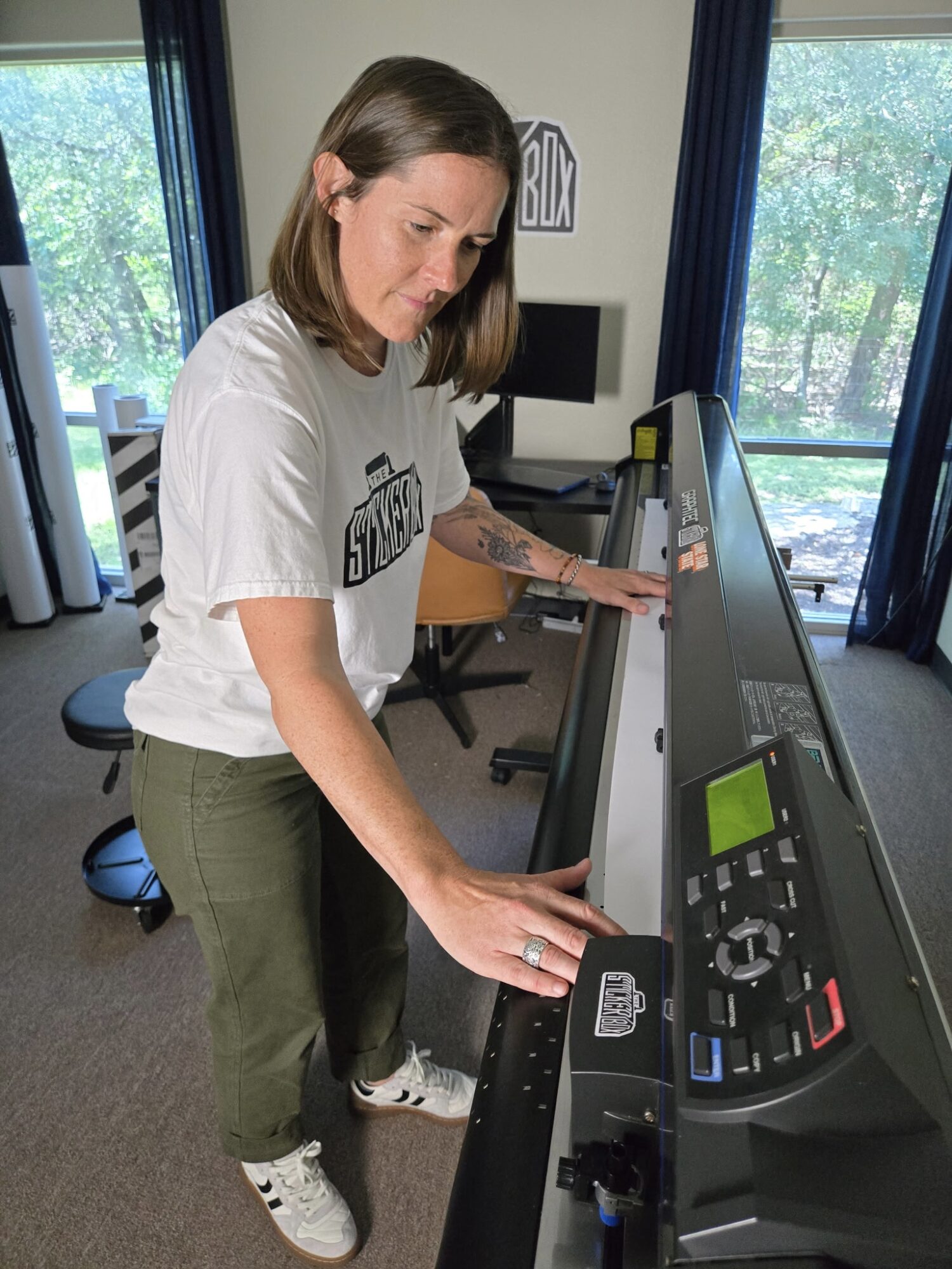 Woman standing at treadmill control panel, adjusting settings, in a room with large windows and blue curtains.