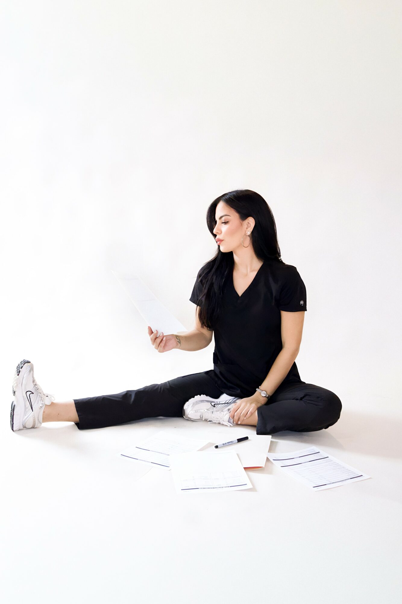 Woman sitting on the floor with papers, stretching her legs, against a plain white background.