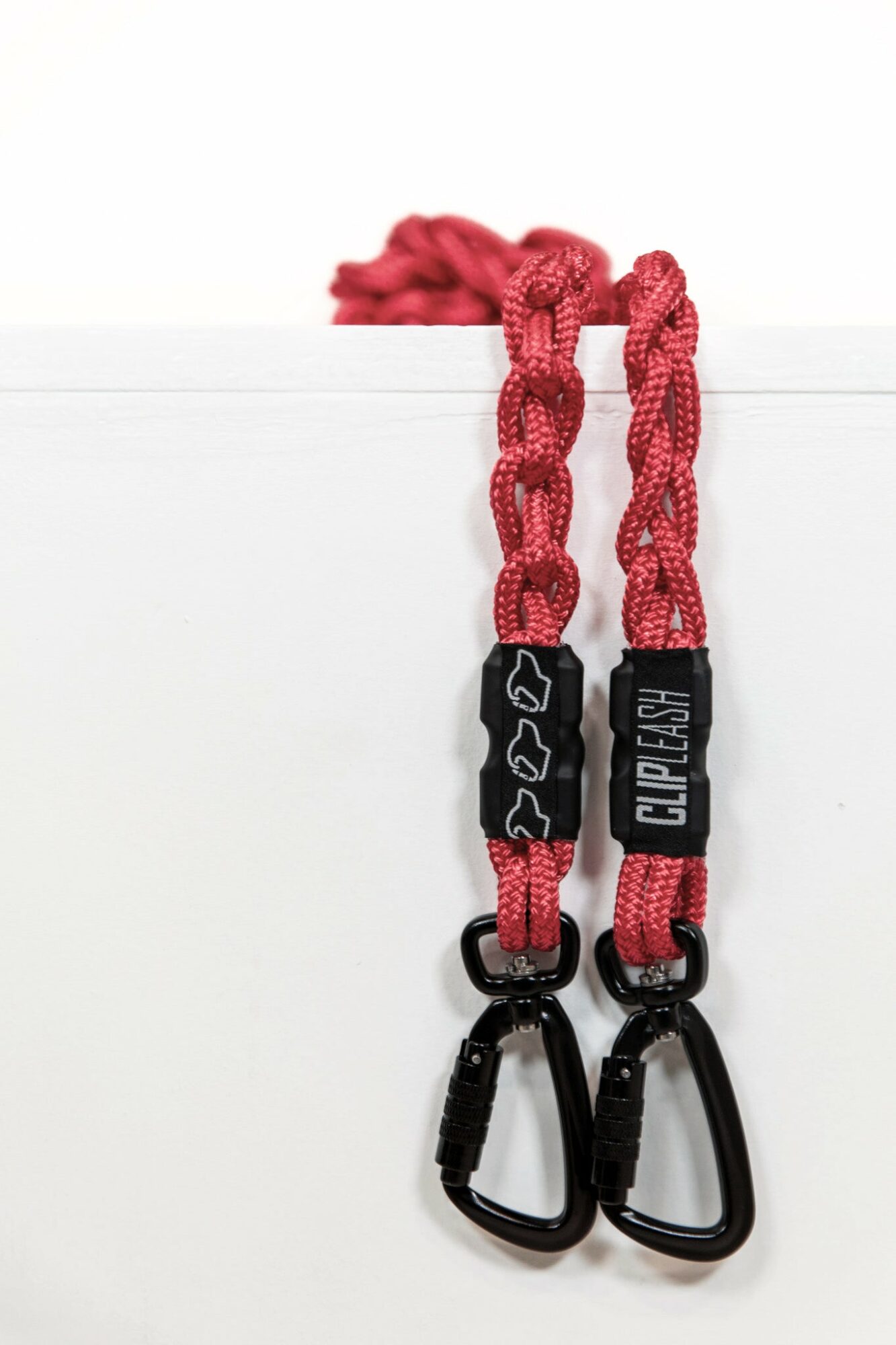 Red and black climbing gear with carabiners and a label, hanging against a white background.