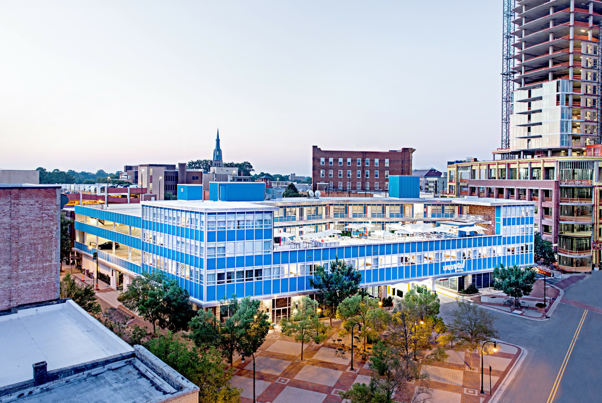 Modern glass building with trees and a cityscape background, viewed from an elevated angle.