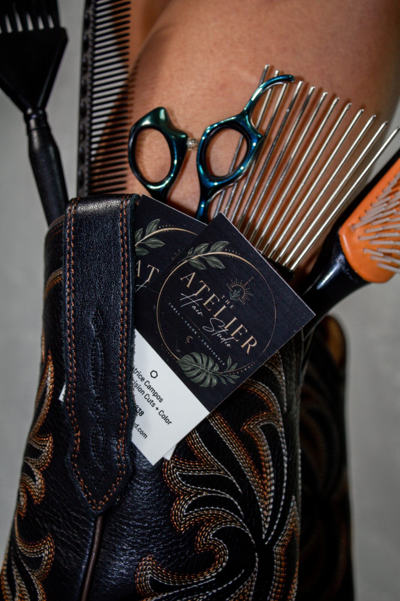Barber tools including scissors, comb, and clipper in a leather pouch, with a business card visible, on a person's leg.