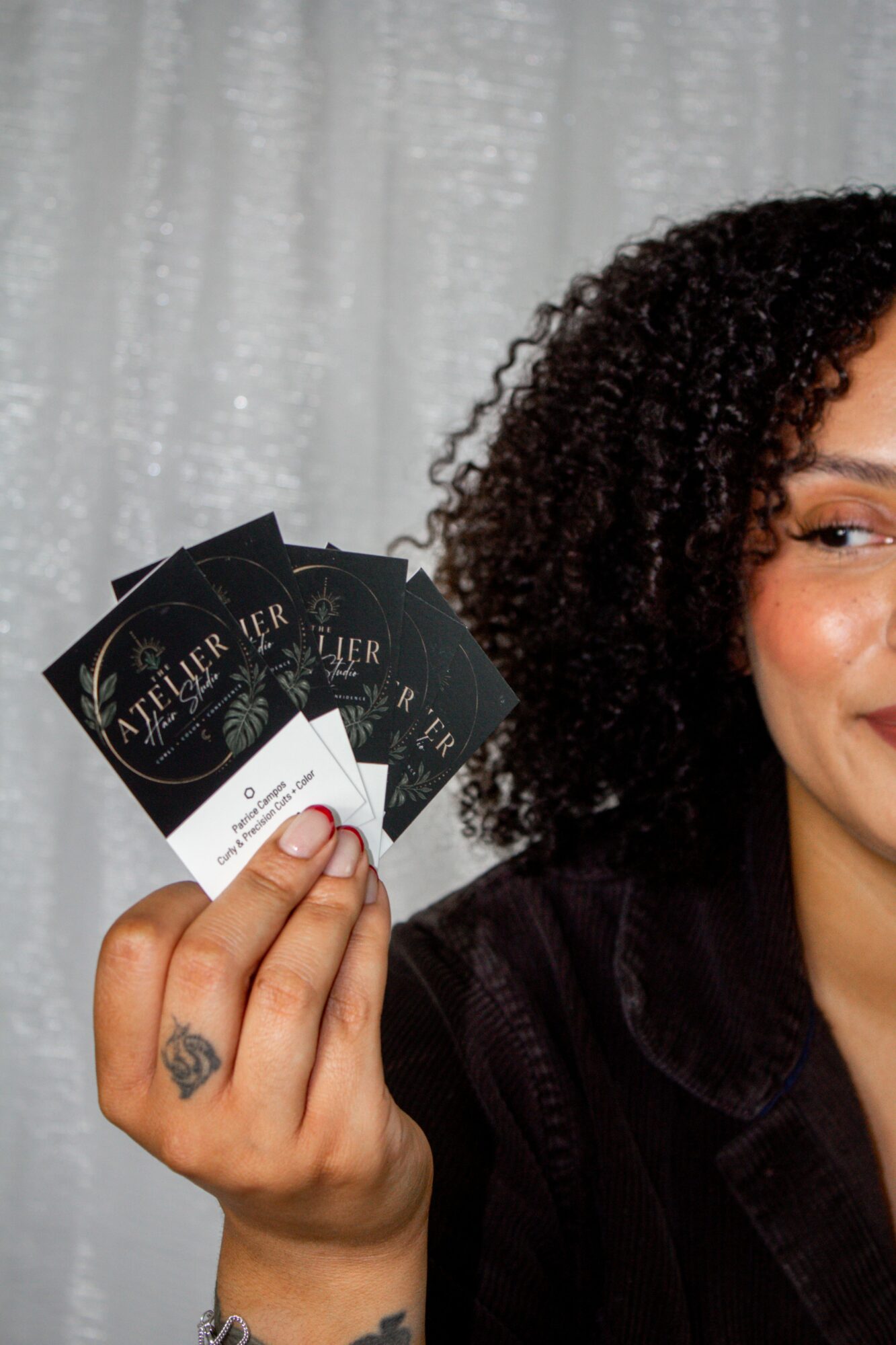 Person with curly hair holding three black cards with white text, smiling, in front of a light curtain background.