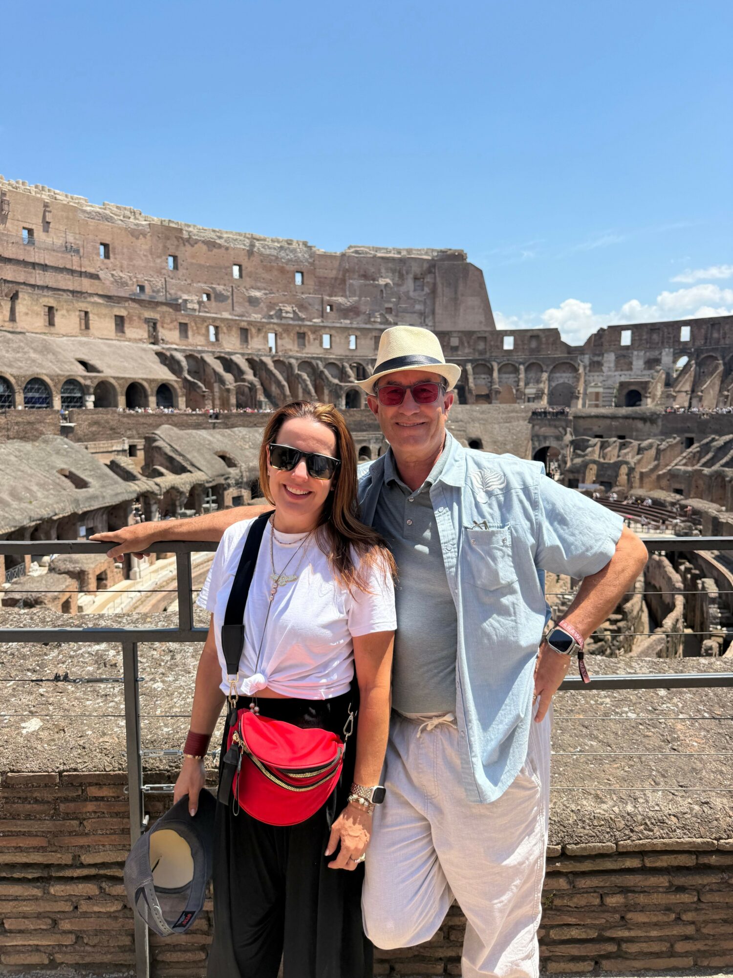 Two people standing on ancient ruins with a cityscape in the background, one wearing a hat and sunglasses, the other with a backpack.