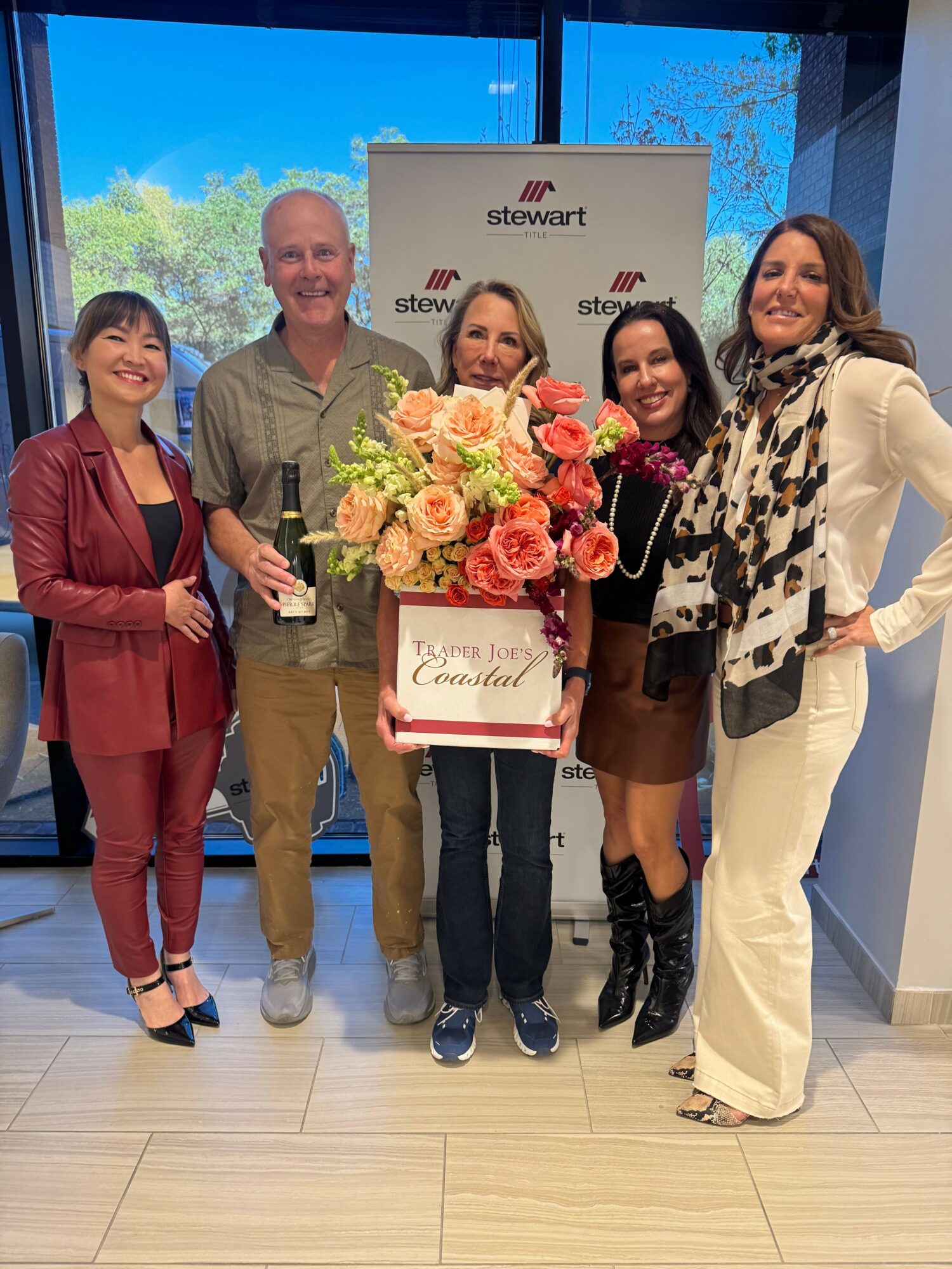 Four people standing indoors, one holding a large bouquet of flowers, with a screen displaying a logo in the background.