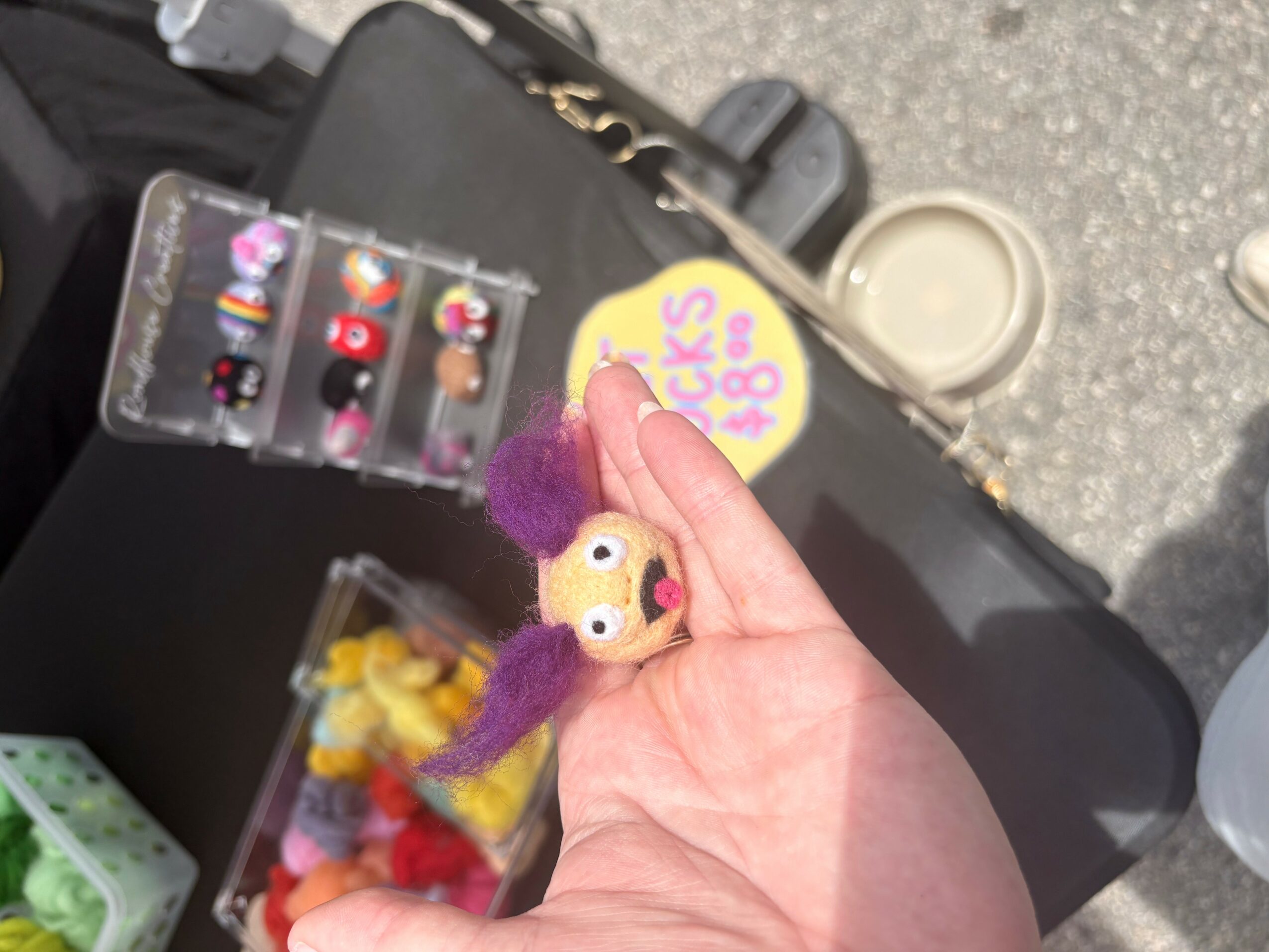 Person holding a small plush toy with purple and yellow colors, with a yellow circular sticker nearby, on a black surface.