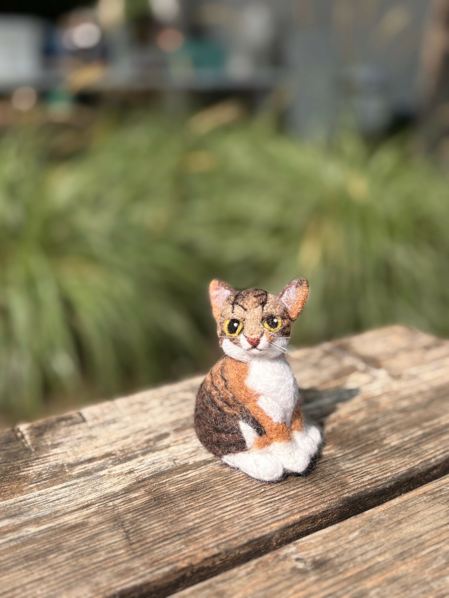 Small animal figurine with large eyes sitting on a wooden surface outdoors, blurred greenery in background.