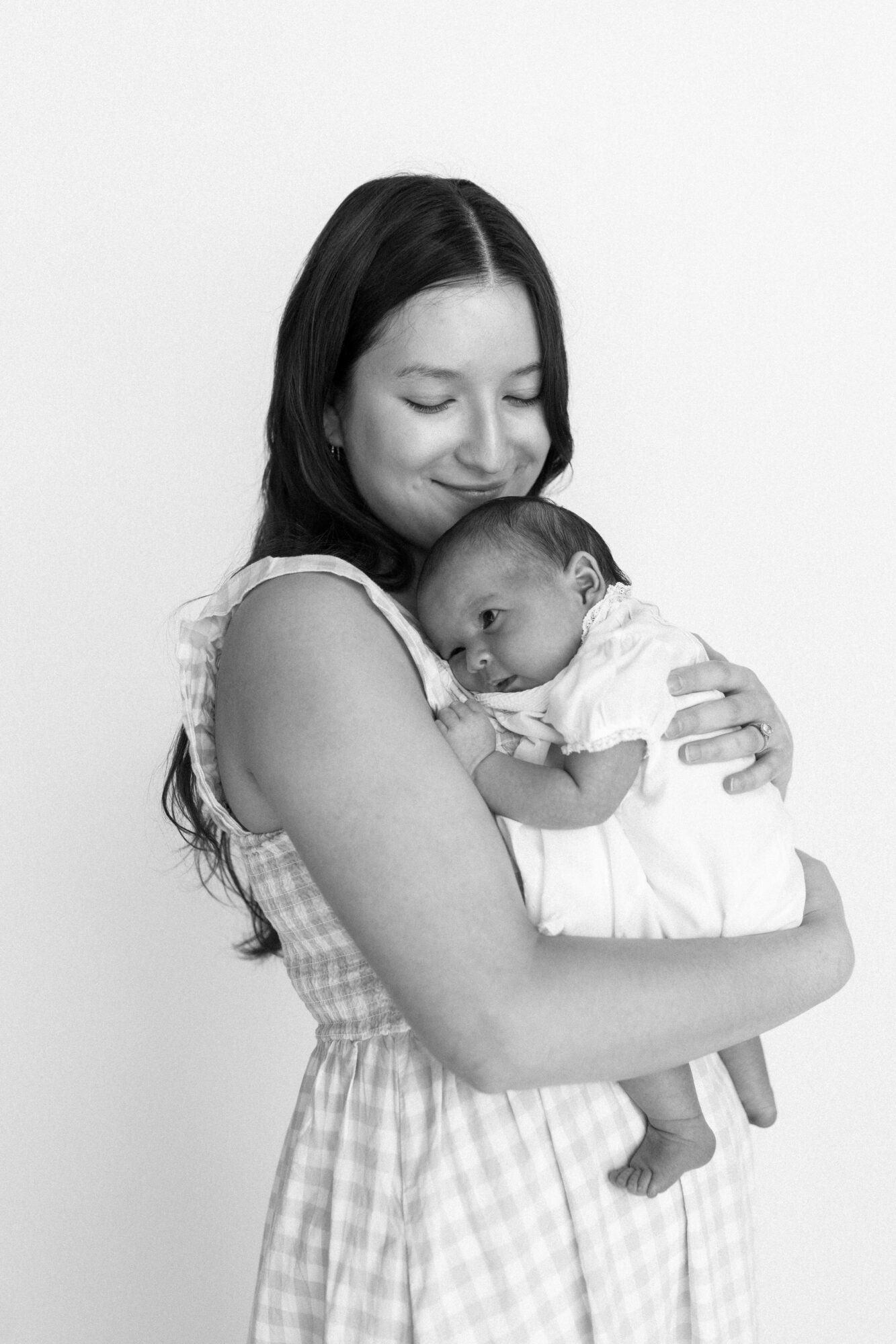 Woman holding a baby close, both smiling gently, against a plain background.