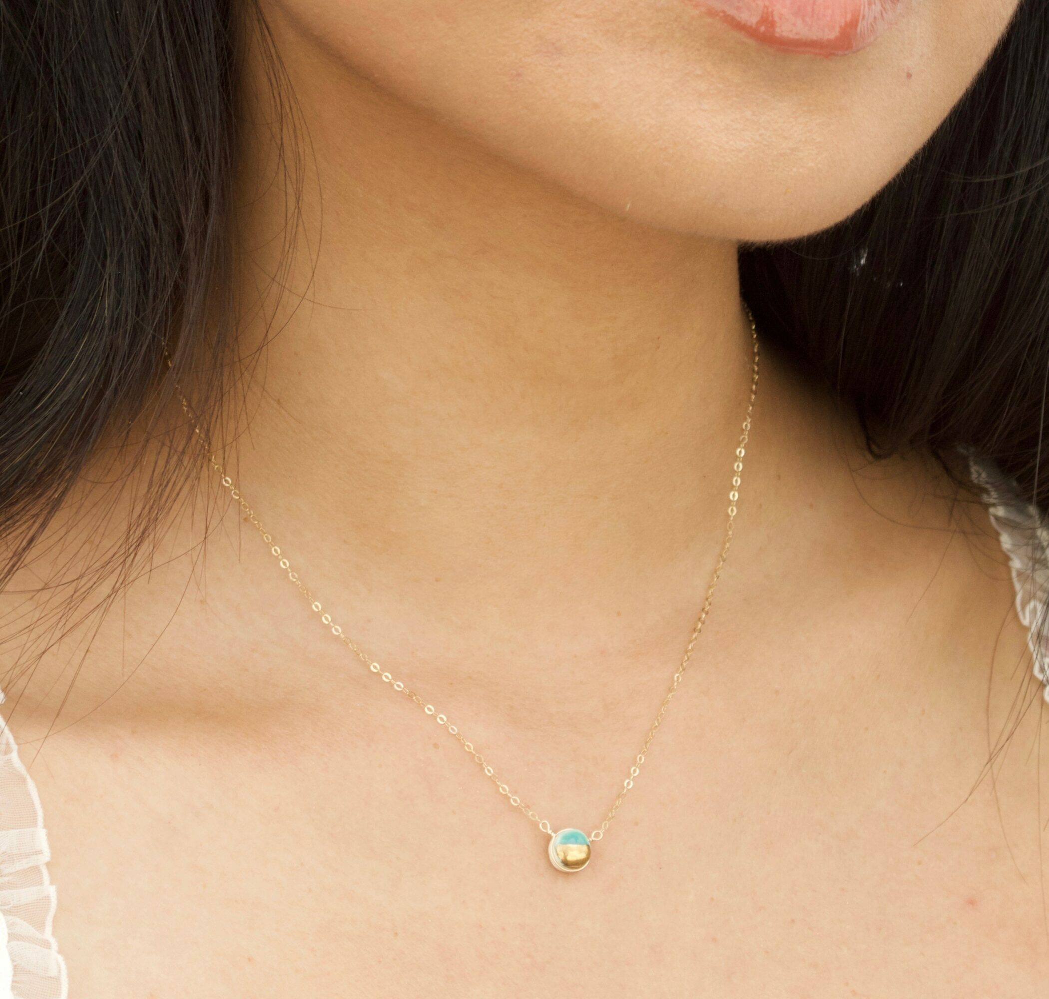 Close-up of a woman's neck wearing a delicate gold necklace with a small pendant, skin and hair visible.