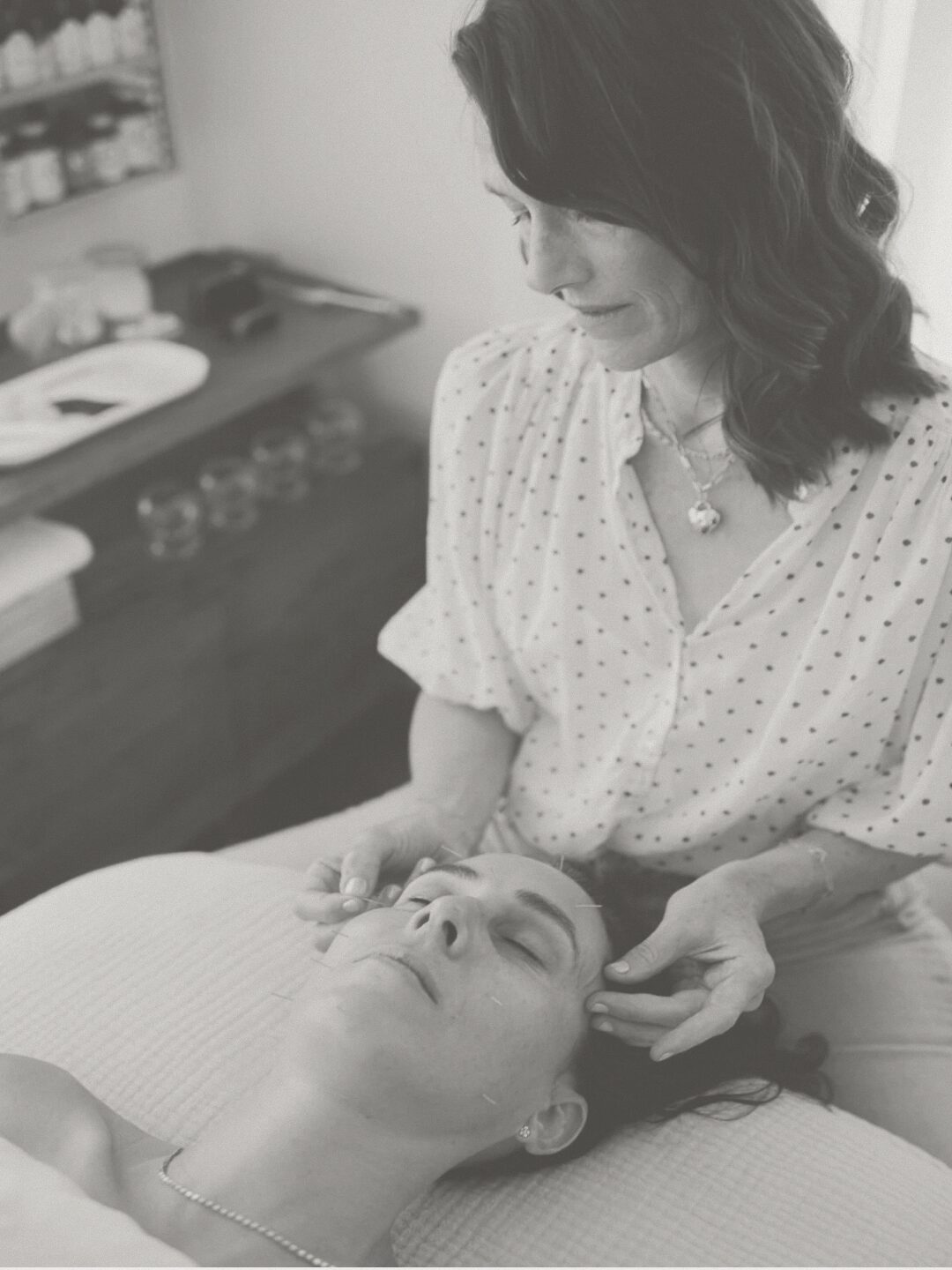 Woman receiving facial treatment from a professional in a clinic, with a calm expression, in black and white.