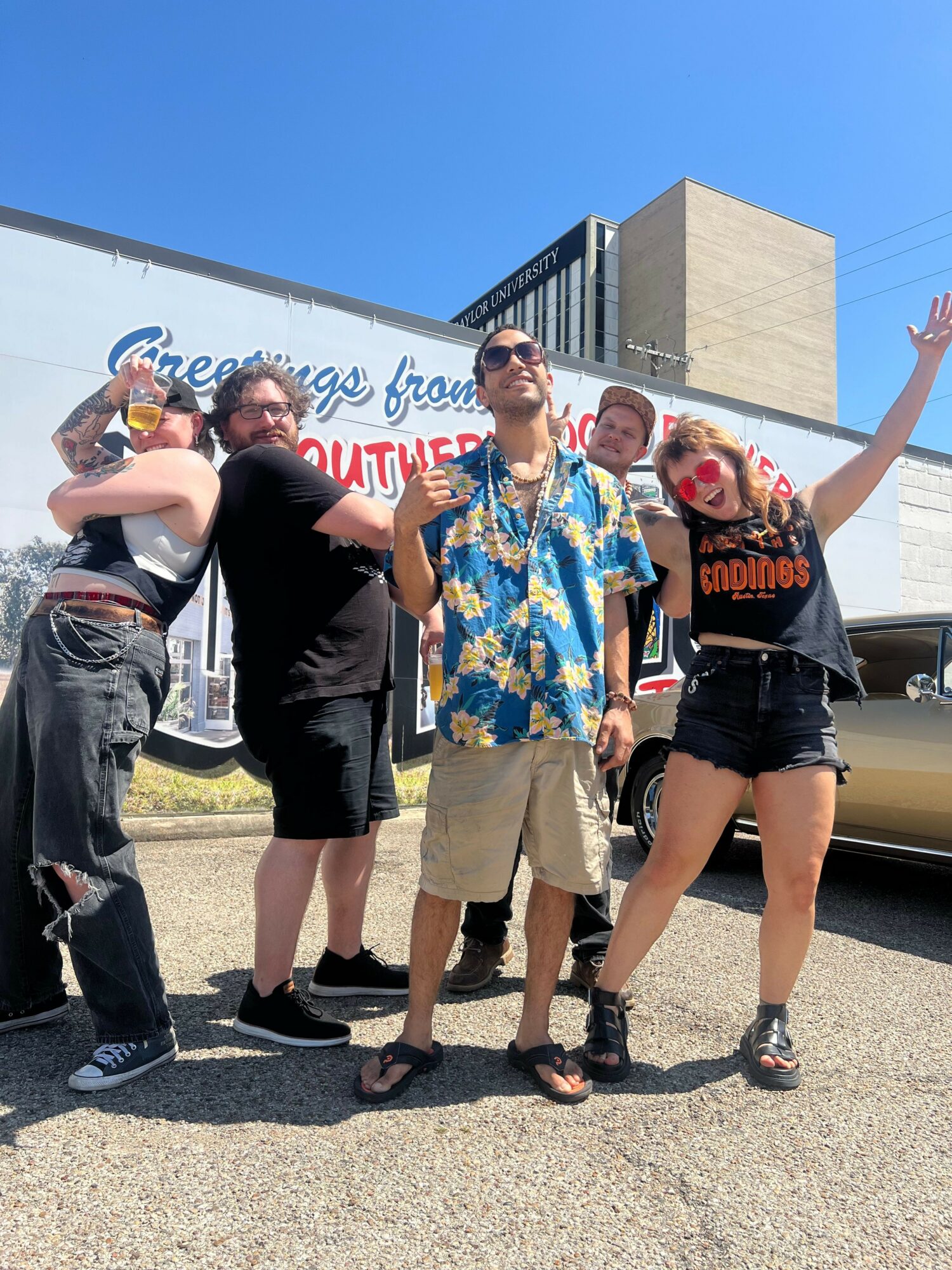 Group of five people standing outdoors, some wearing masks, with a building and a sign in the background.