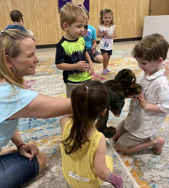 Children and an adult playing with a dog on a colorful carpet in a room with wooden walls.