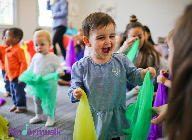 Children holding colorful scarves in a classroom, smiling and playing together.