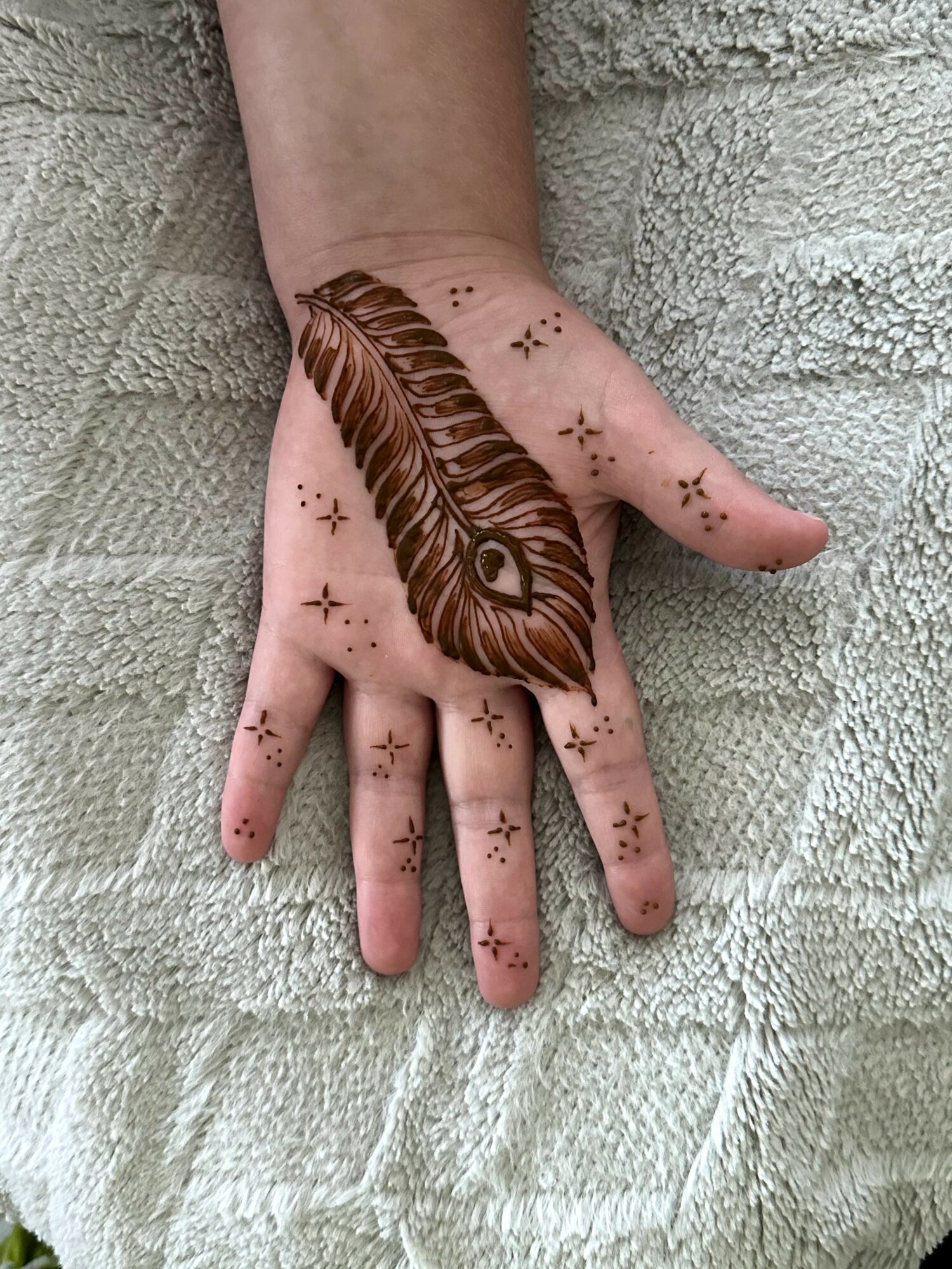 Hand with a feather tattoo and small star and dot designs, resting on a textured light-colored surface.