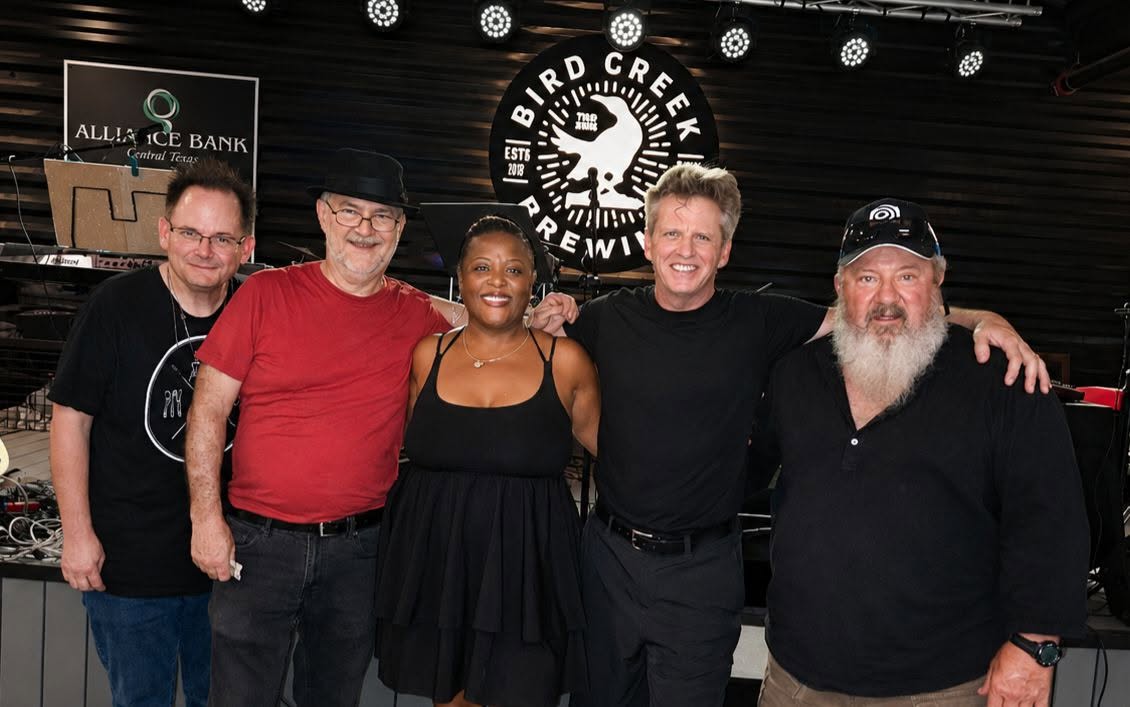 Five people standing together in front of a sign that says Bird Creek Brewery, smiling and posing for the photo.