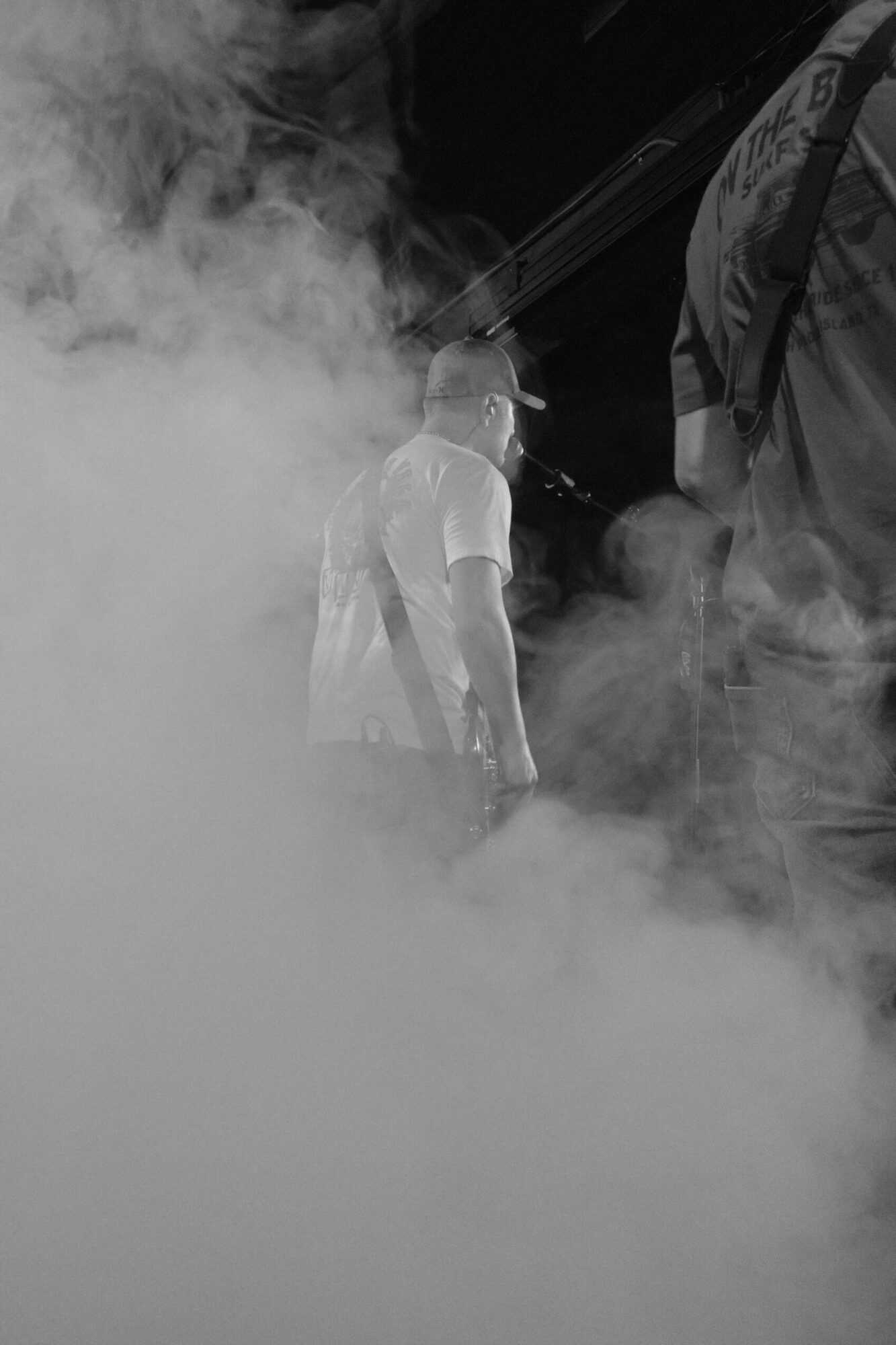 Person holding a device emitting thick smoke or vapor, with a dark background, possibly indoors.