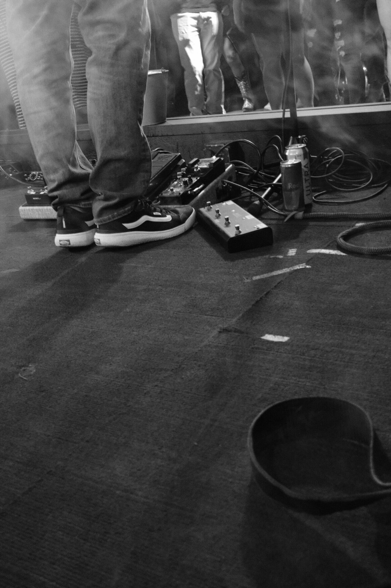 People standing on a stage with equipment, shoes, and cables on the floor, viewed from the side.