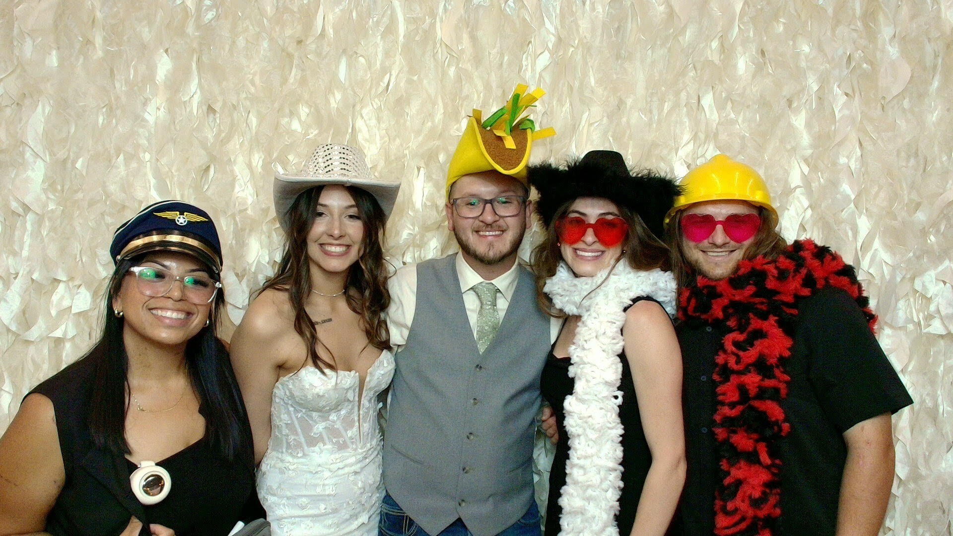 Group of five people dressed in costumes and accessories, smiling, standing in front of a textured beige background.