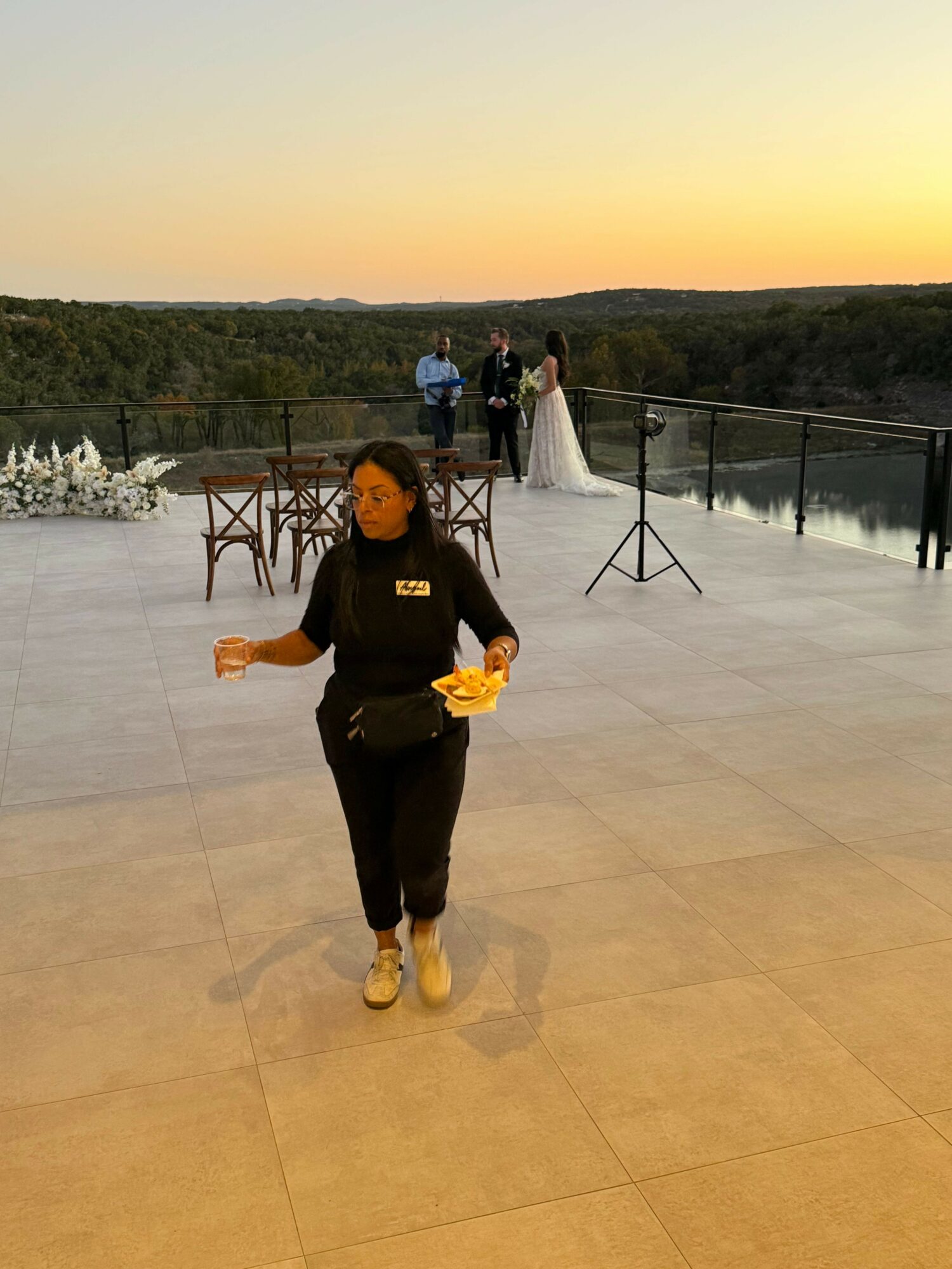 Person walking on a terrace during sunset, with a sunset sky and trees in the background.