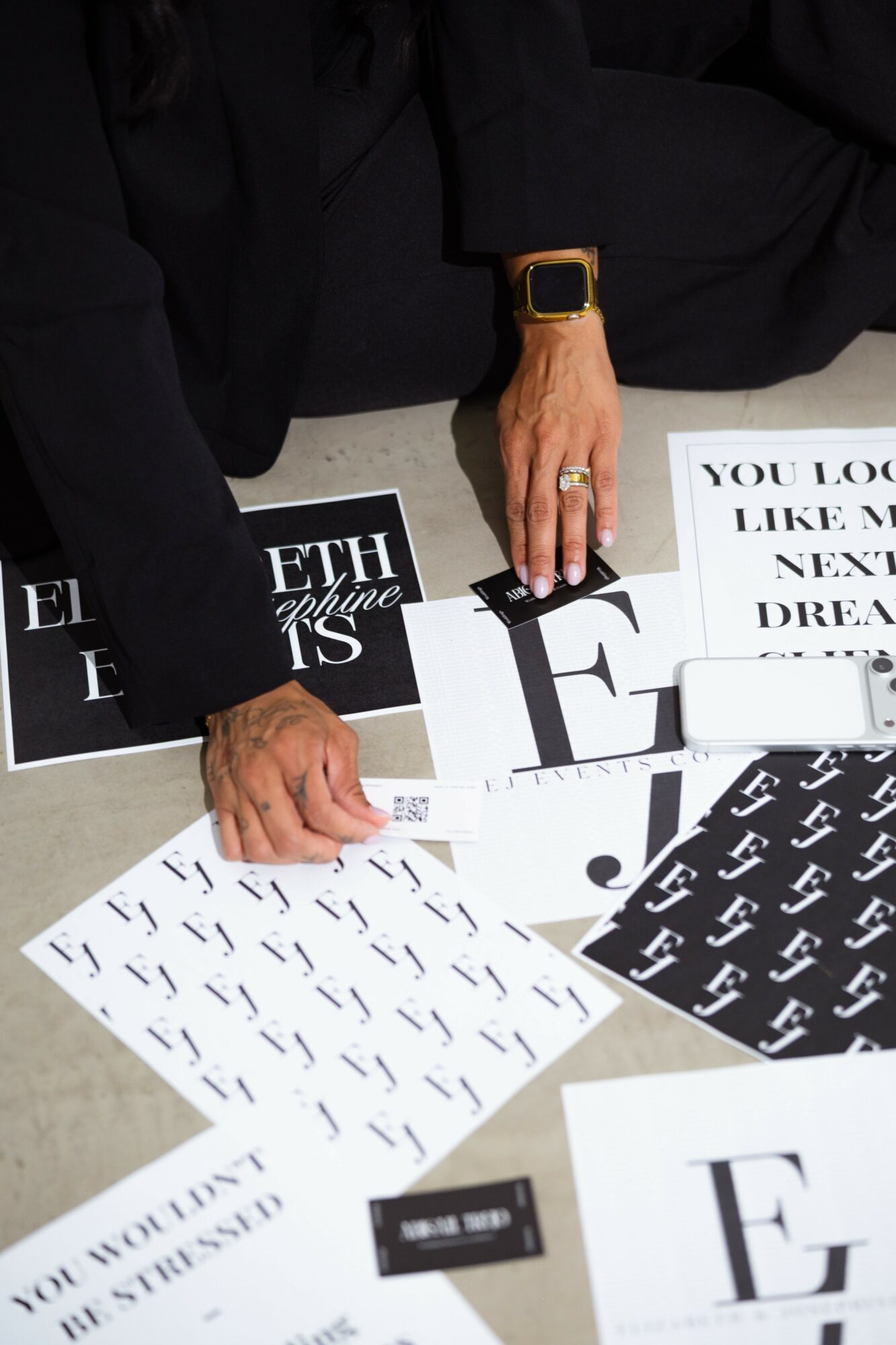 Person's hand with rings and watch, surrounded by black and white printed papers on a table.