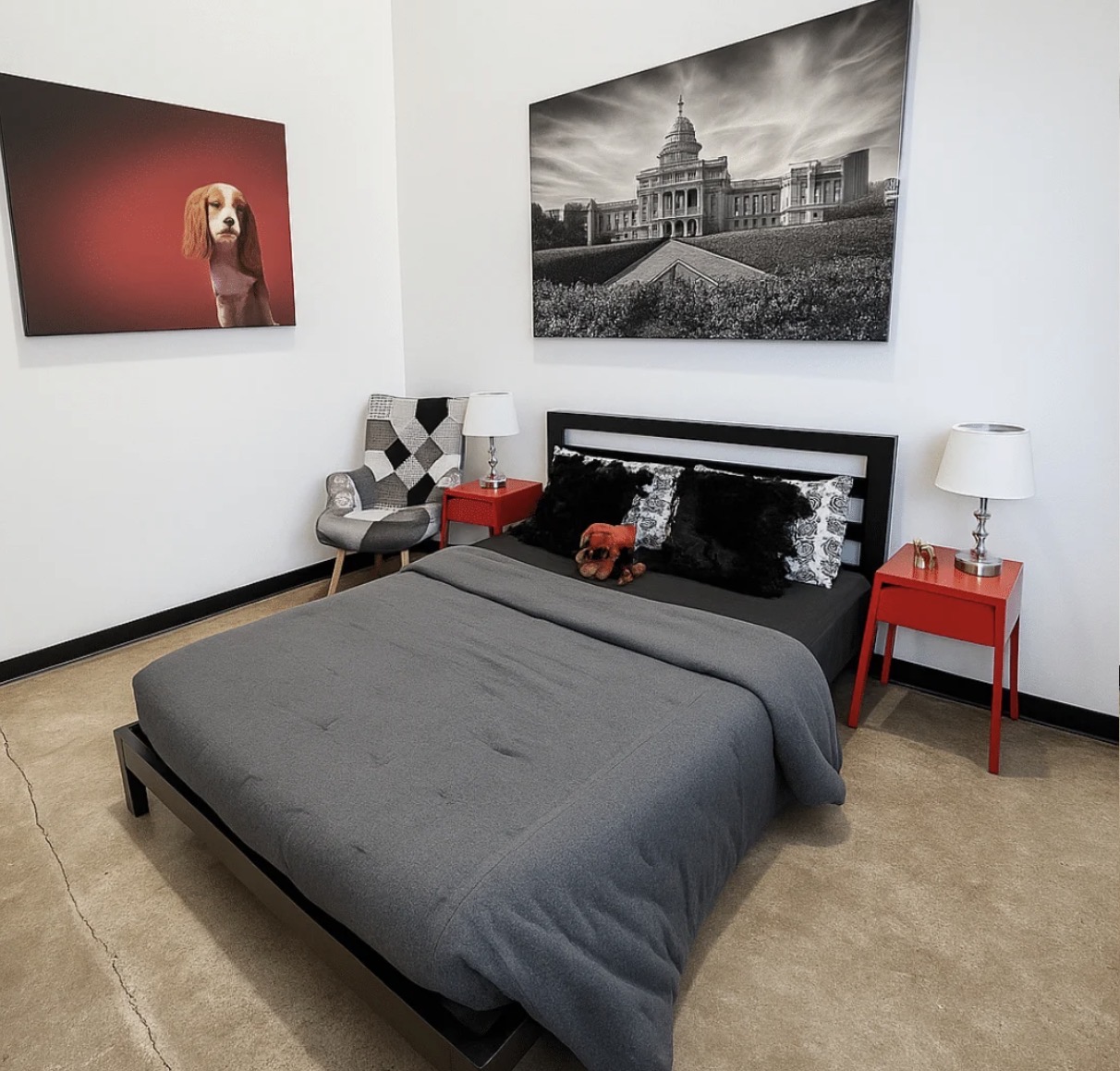 Bedroom with a bed, two red nightstands, a gray blanket, and wall art including a dog portrait and a cityscape.