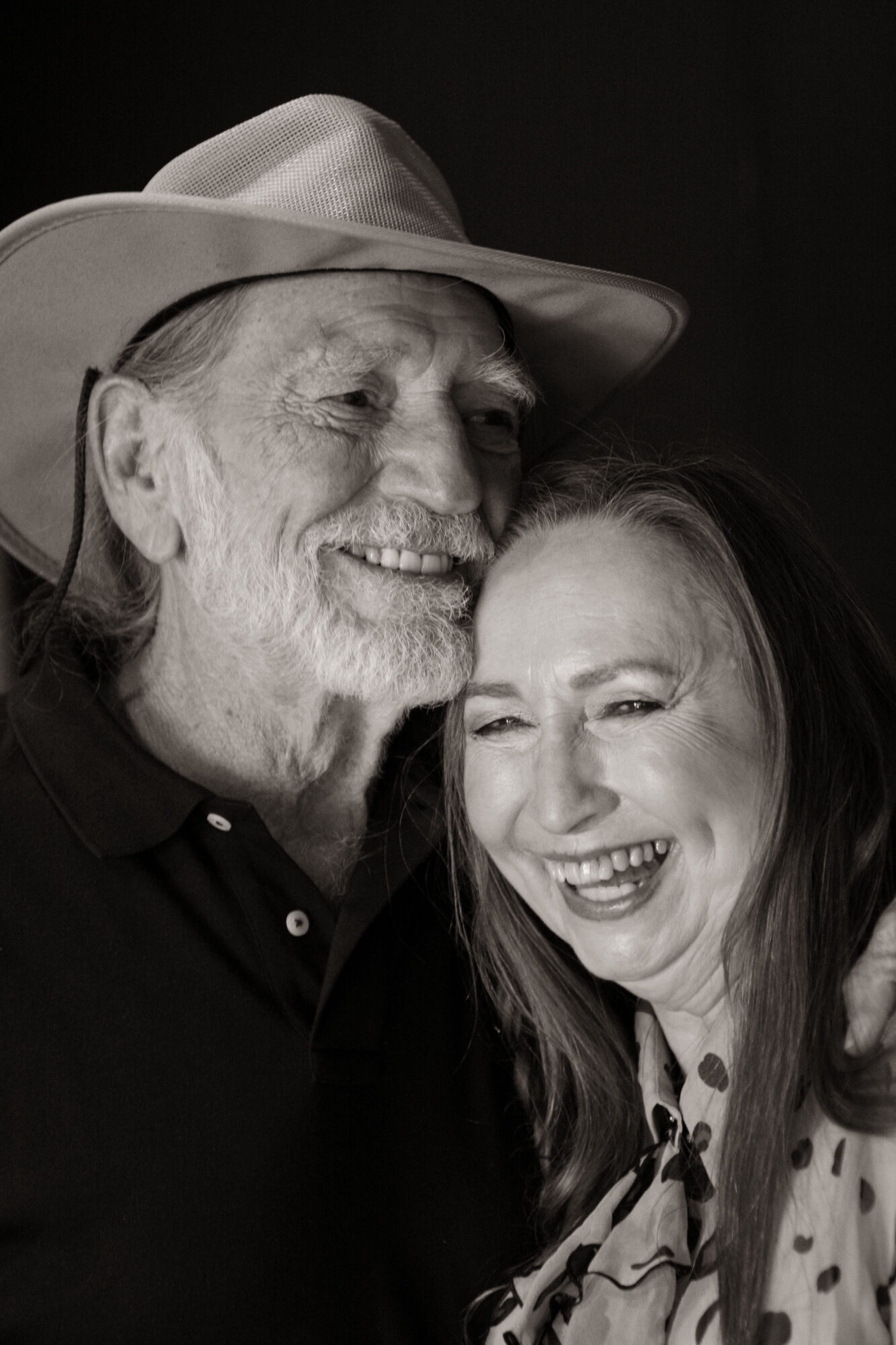 An elderly man with a beard and a hat smiling next to a woman with long hair, both smiling.