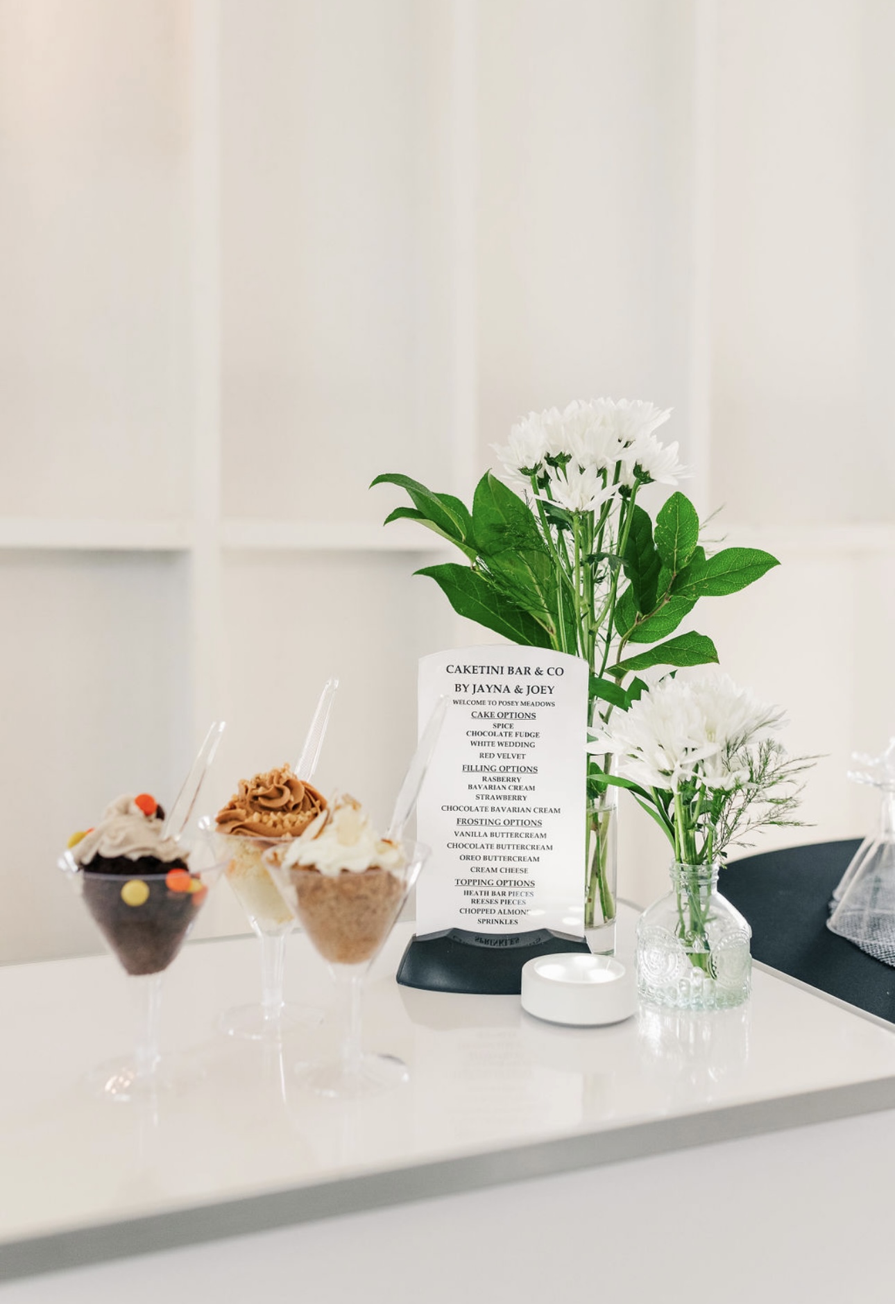 Flowers in a glass vase, cupcakes, and a menu on a white table with a light background.