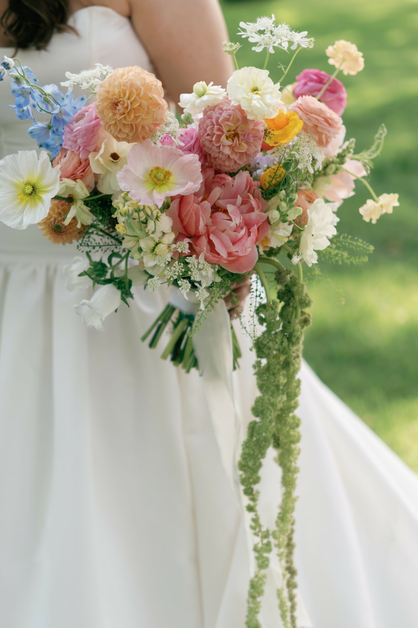 Person in white dress holding a large colorful bouquet of flowers outdoors, with green background.